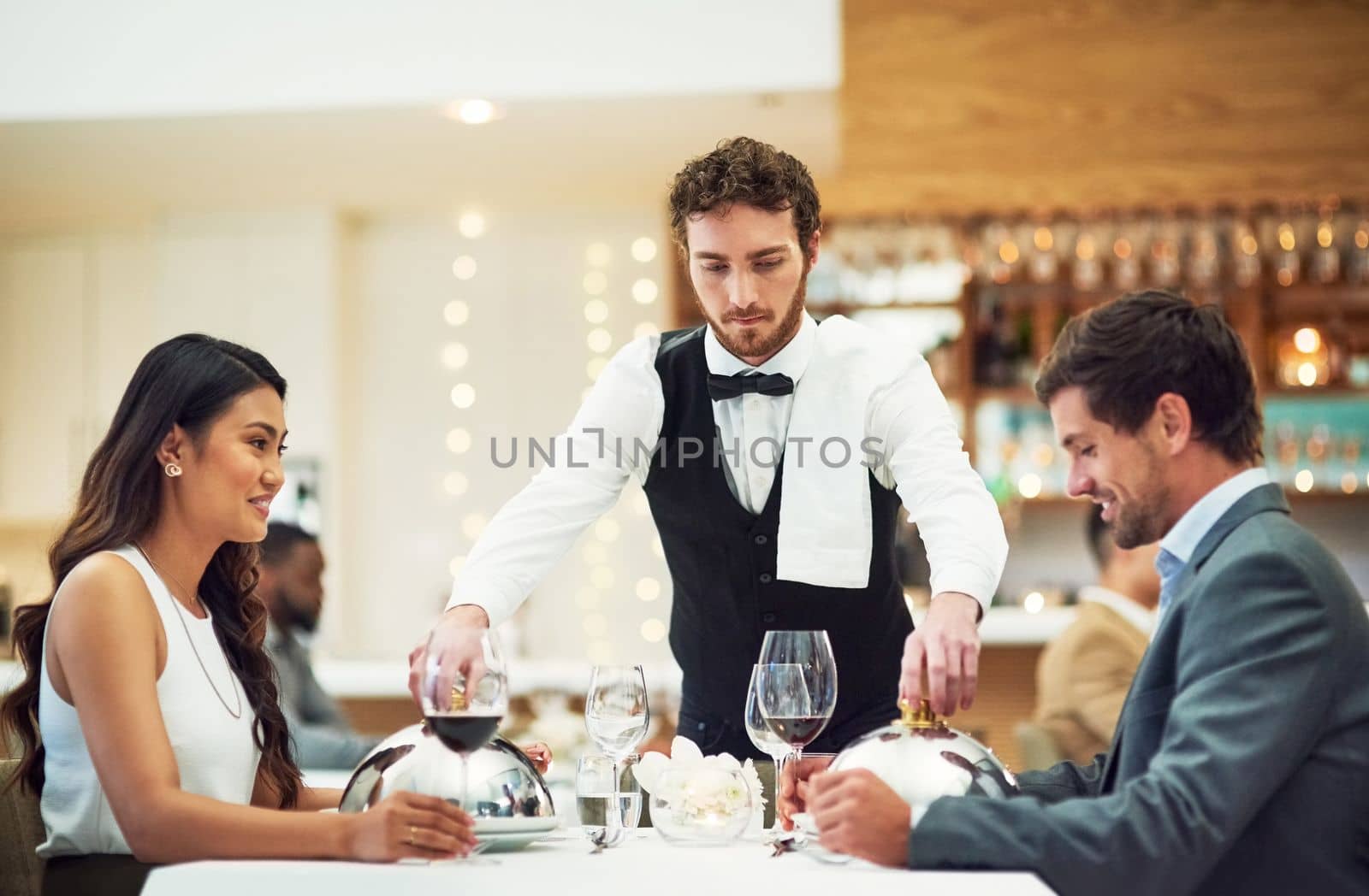 Couple, restaurant server and fine dining at table for valentines day date, bonding and romance in night. Man, woman and waiter with food, service and hospitality for dinner, love and celebration.