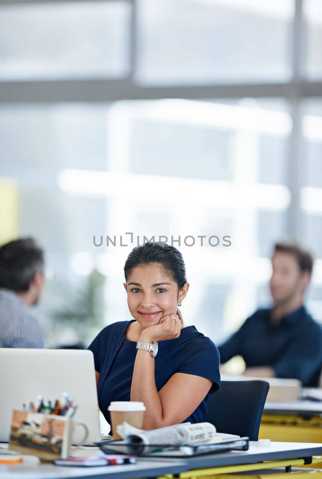 Work couldnt be better. Portrait of a designer sitting at her desk working on a laptop with colleagues in the background