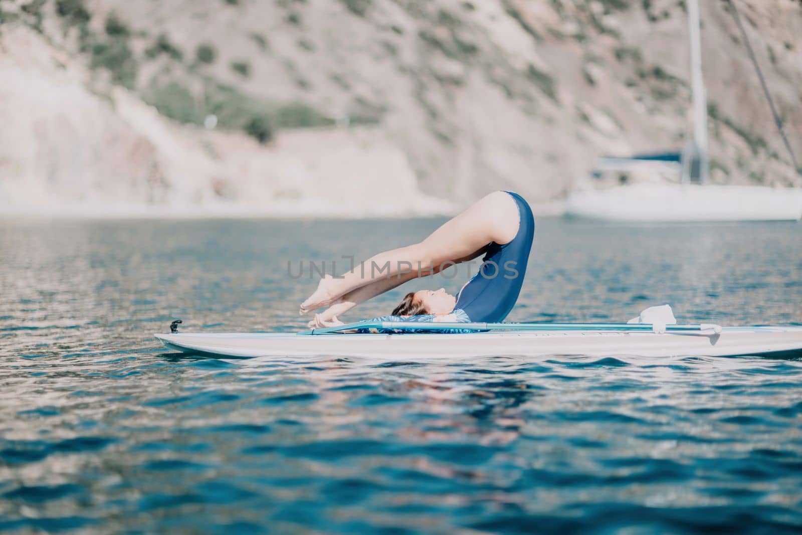 Woman sup yoga. Middle age sporty woman practising yoga pilates on paddle sup surfboard. Female stretching doing workout on sea water. Modern individual hipster outdoor summer sport activity