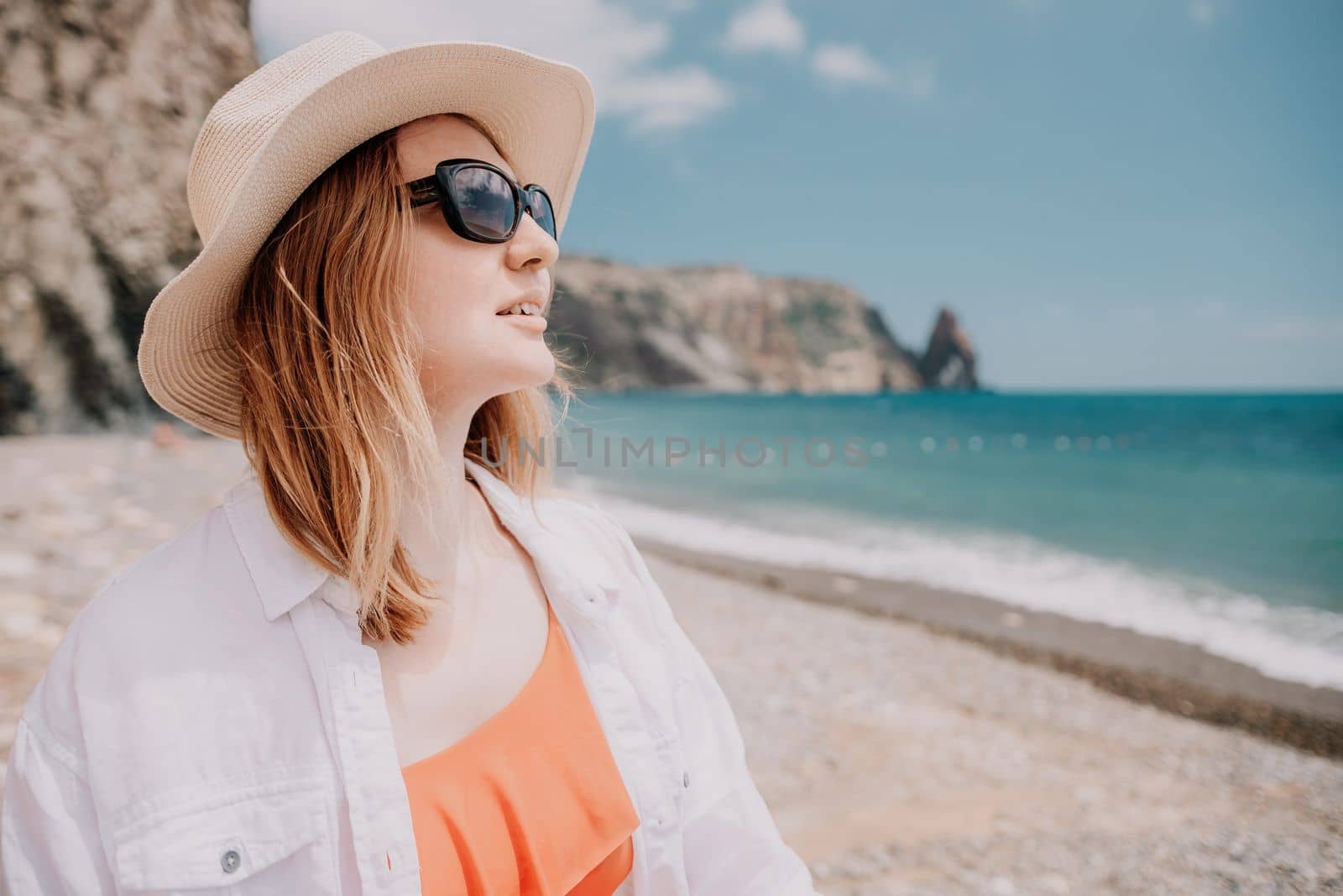 Young woman in red bikini on Beach. Blonde in sunglasses on pebble beach enjoying sun. Happy lady in one piece red swimsuit relaxing and sunbathing by turquoise sea ocean on hot summer day. Close up,
