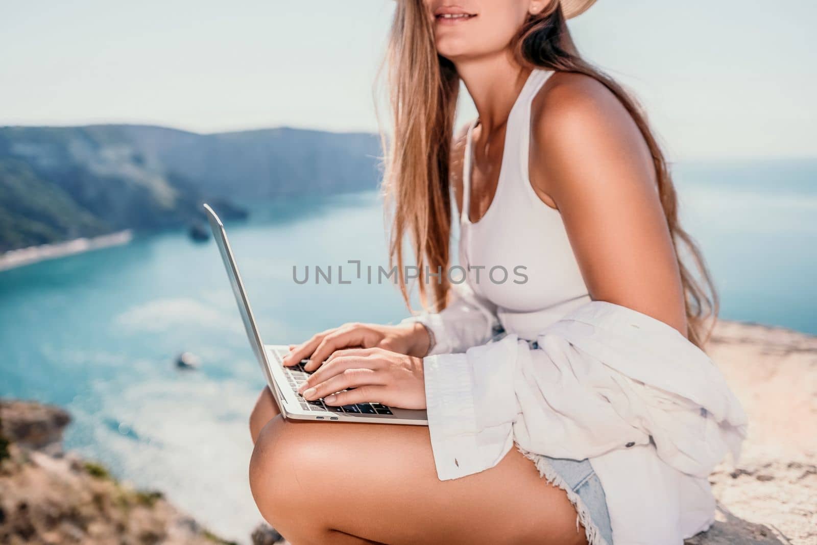 Digital nomad, Business woman working on laptop by the sea. Pretty lady typing on computer by the sea at sunset, makes a business transaction online from a distance. Freelance remote work on vacation