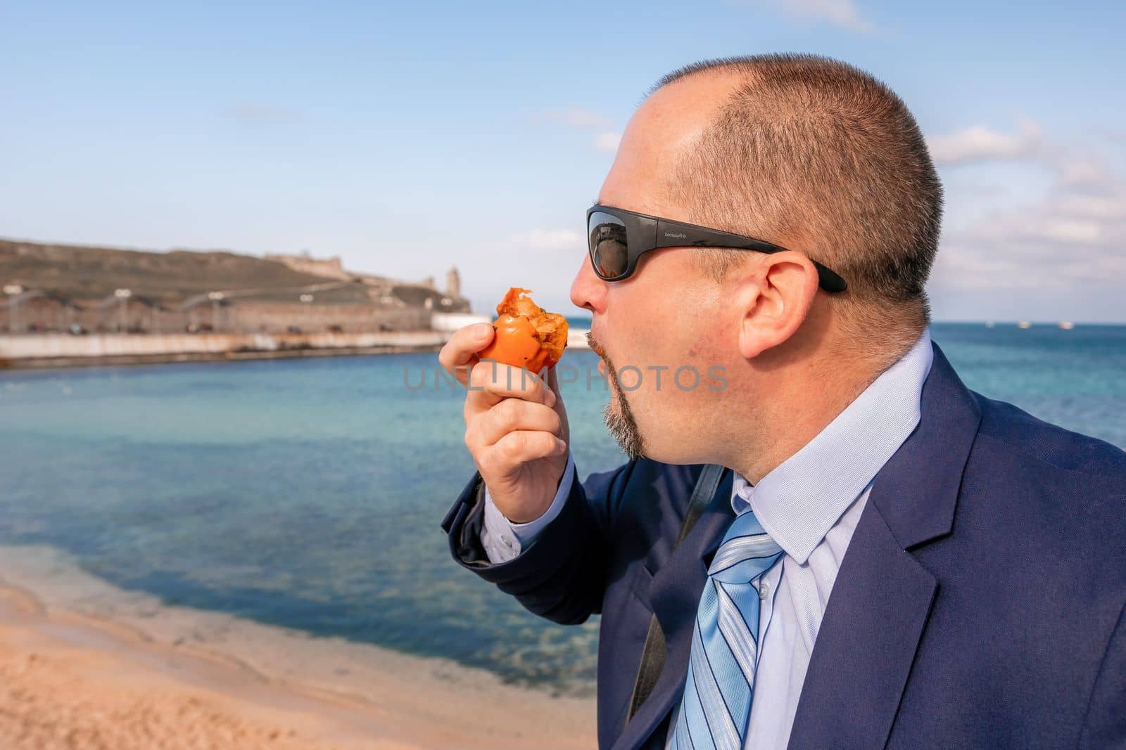 Male persimmon park. Hipster millennial man in a tie and jacket bites off a persimmon while sitting on a park bench in slow motion Young business people eat golden persimmons at lunchtime