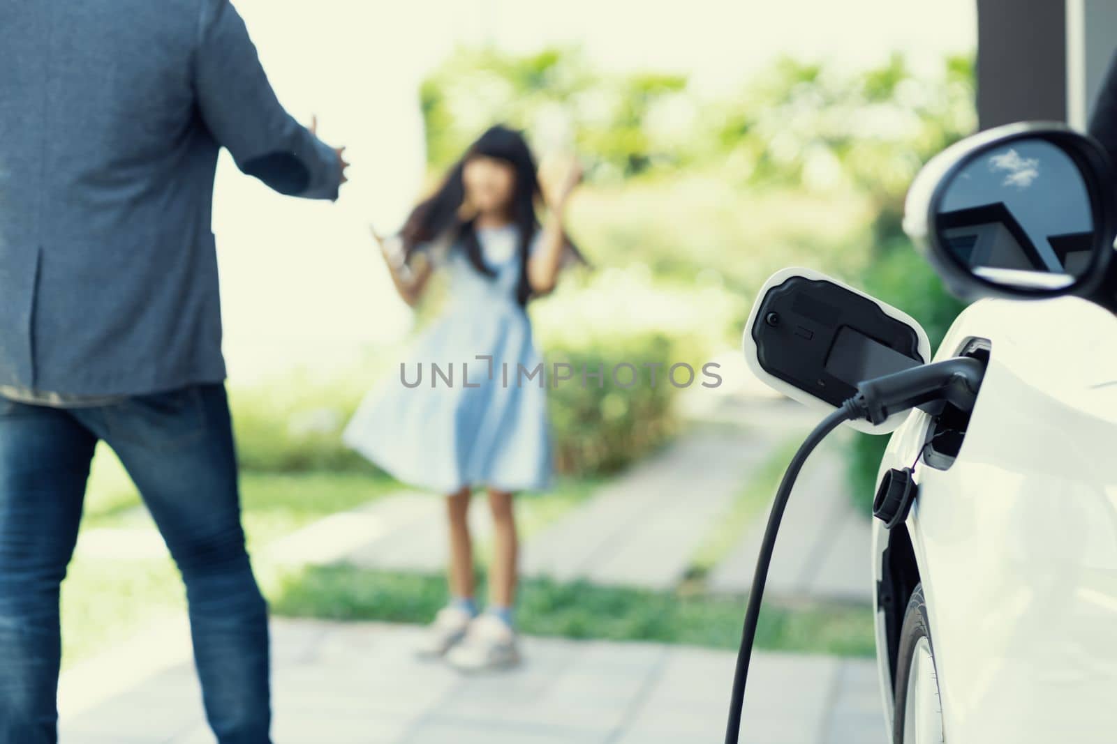 Progressive father and daughter plugs EV charger from home charging station to electric vehicle. Future eco-friendly car with EV cars powered by renewable source of clean energy.