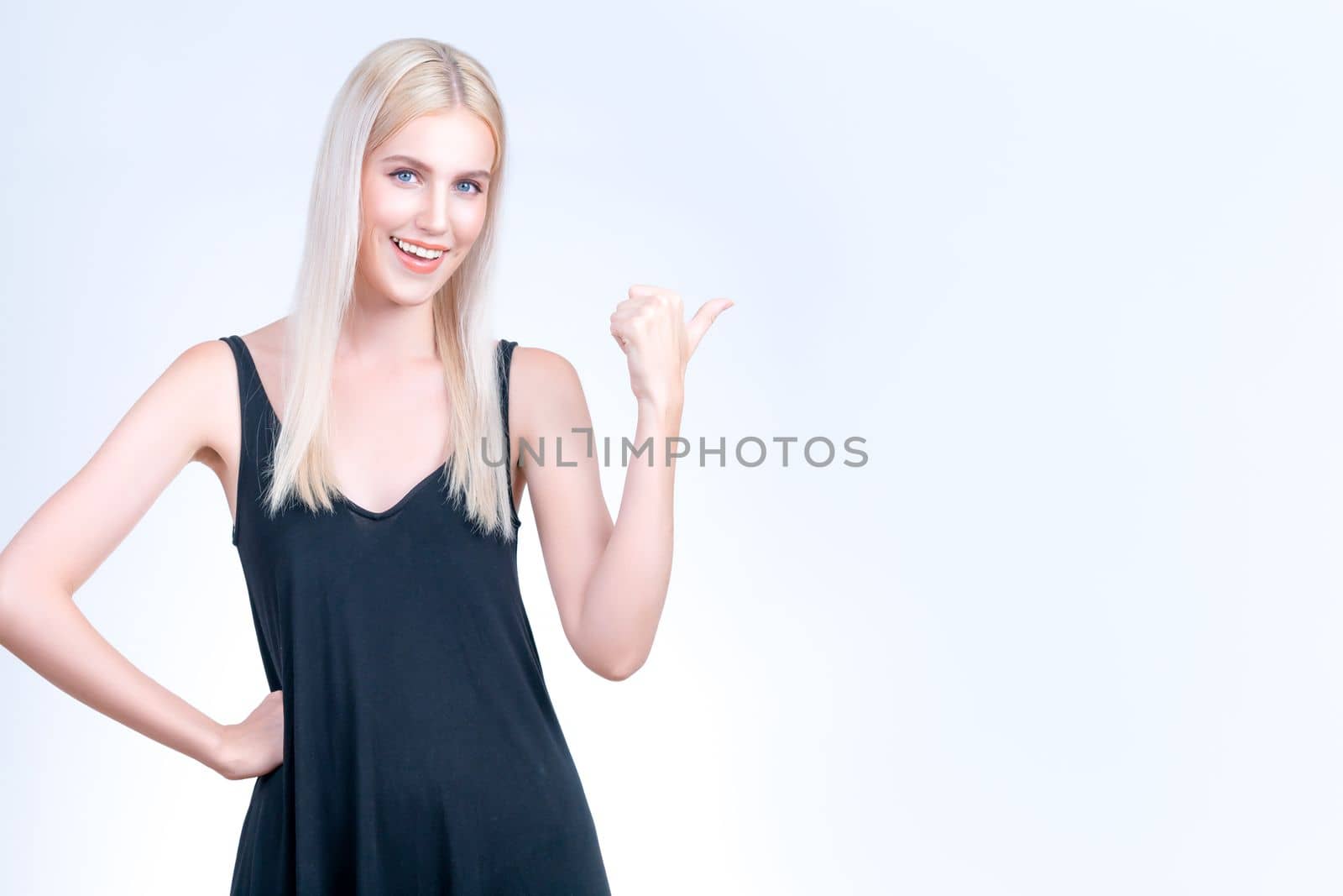 Personable beautiful woman with perfect makeup clean skin pointing finger in copyspace isolated background. Promotion indicated by hand gesture to show skincare product advertising.