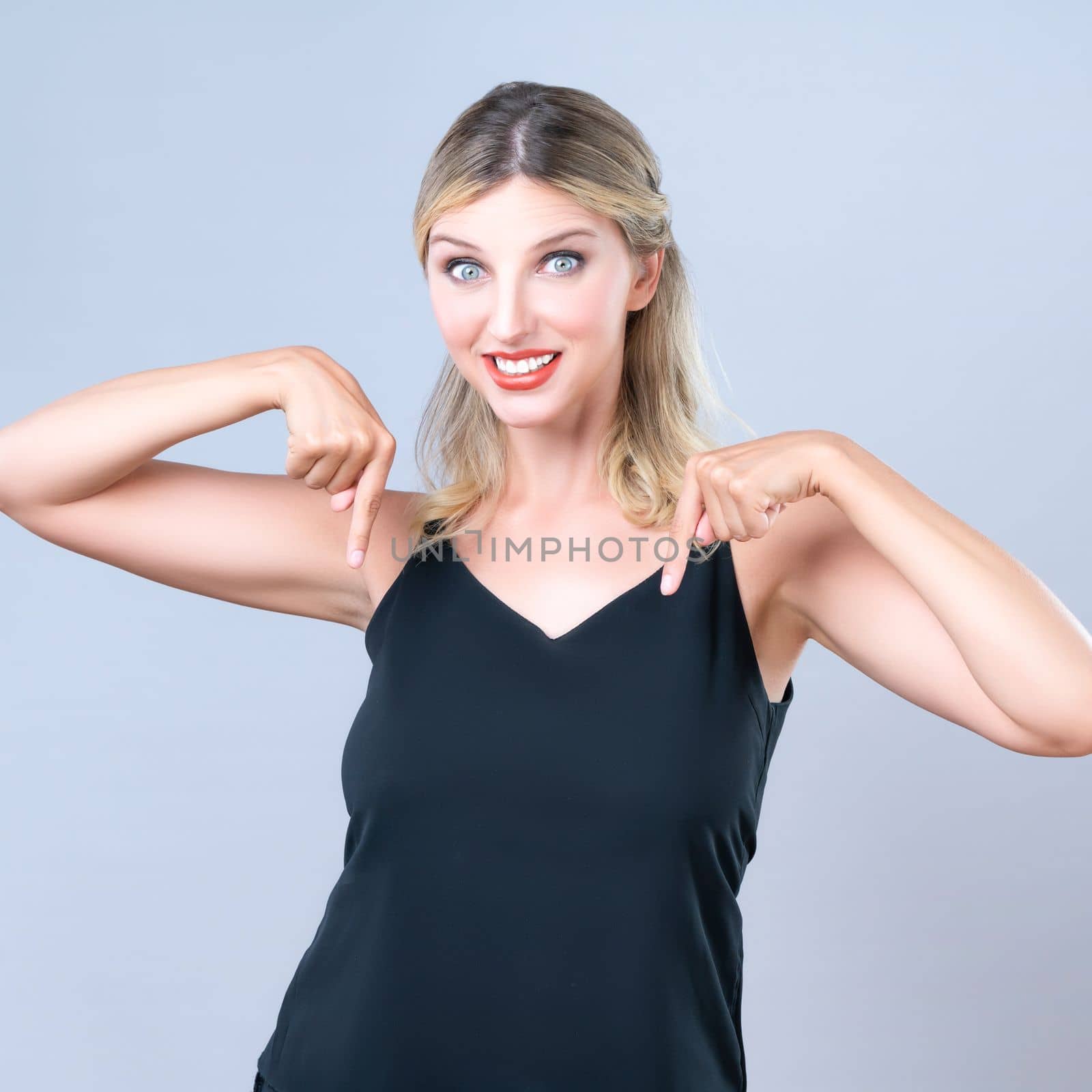 Alluring portrait of beautiful woman with perfect makeup and flawless clean skin pointing finger down in isolated background. Promotion indicated by hand gesture concept for advertisement.
