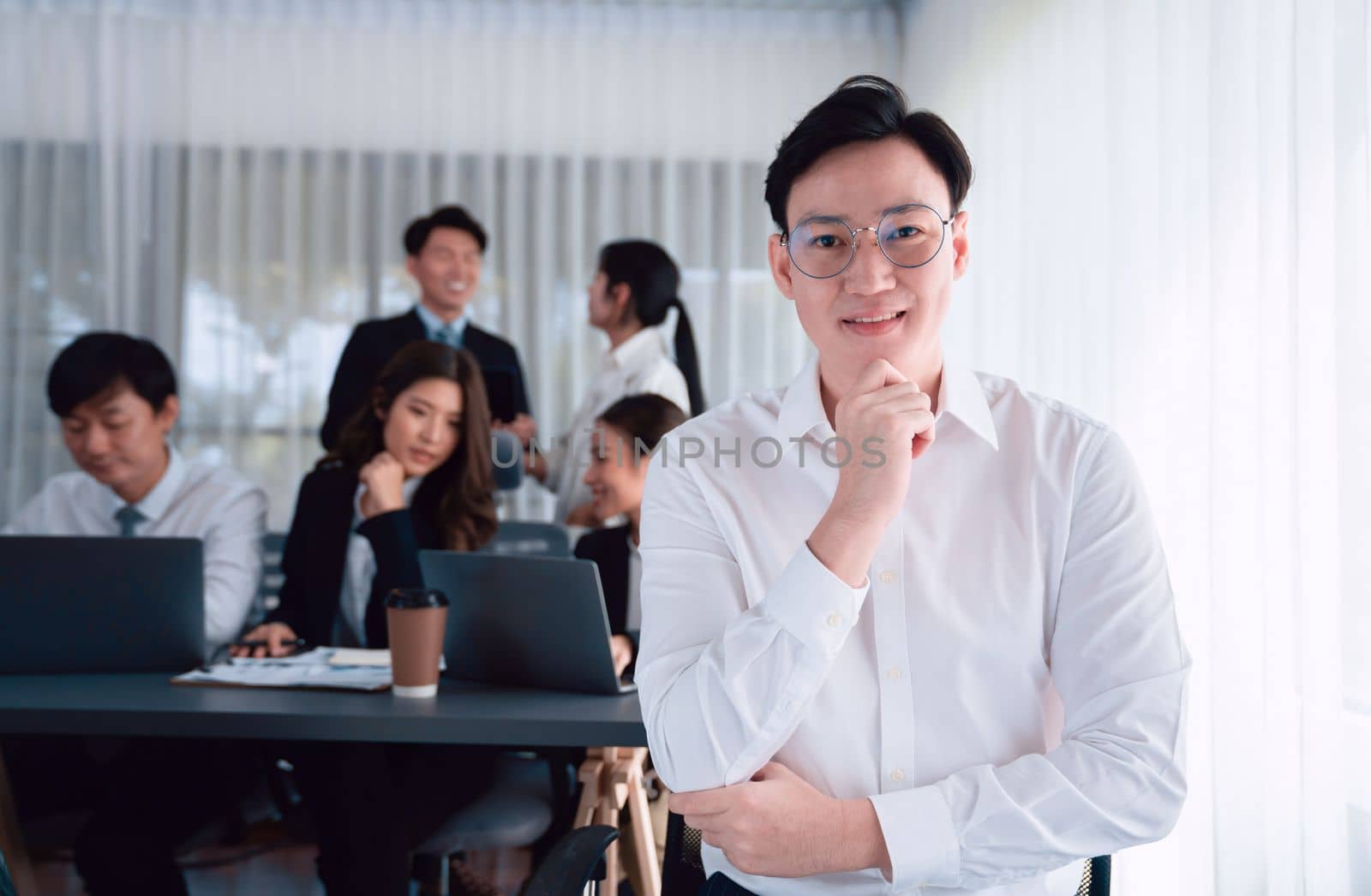 Portrait of focus young successful confident male manager, executive wearing business wear in harmony office arm crossed with blurred meeting background of colleagues, office worker.