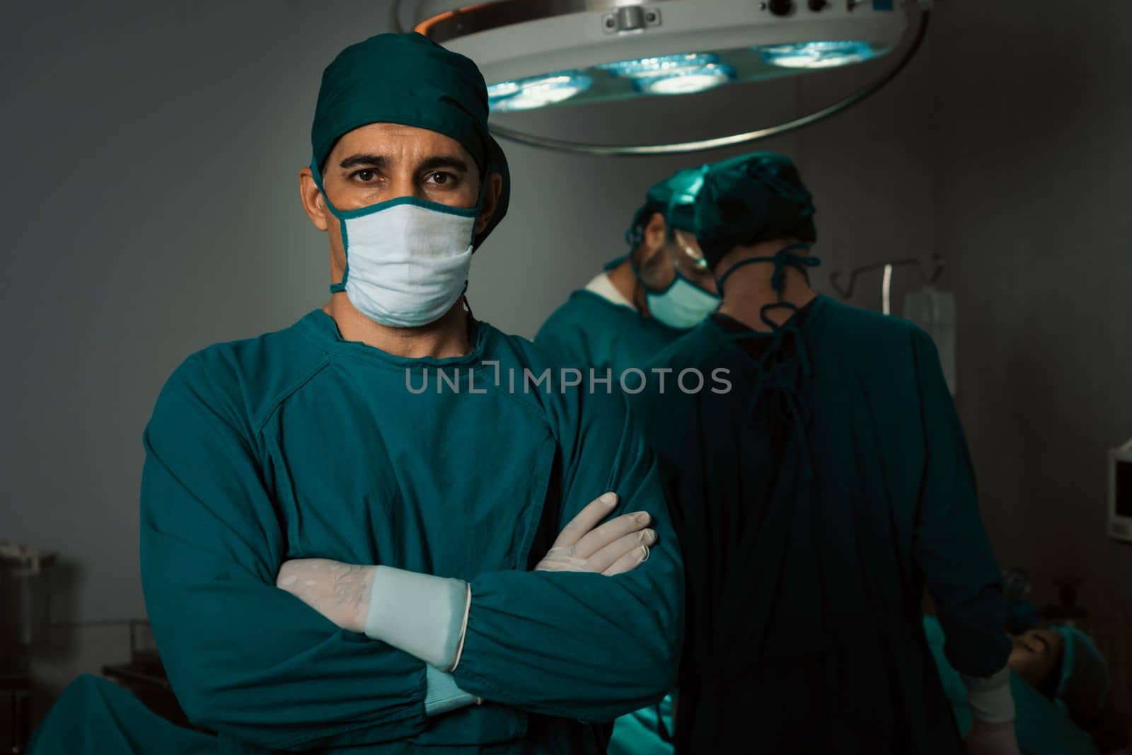 Portrait of surgical team leader in sterile operating room with his team and patient undergoing surgery. Confident and professional surgeon in full protective wear provide medical care to his patient.
