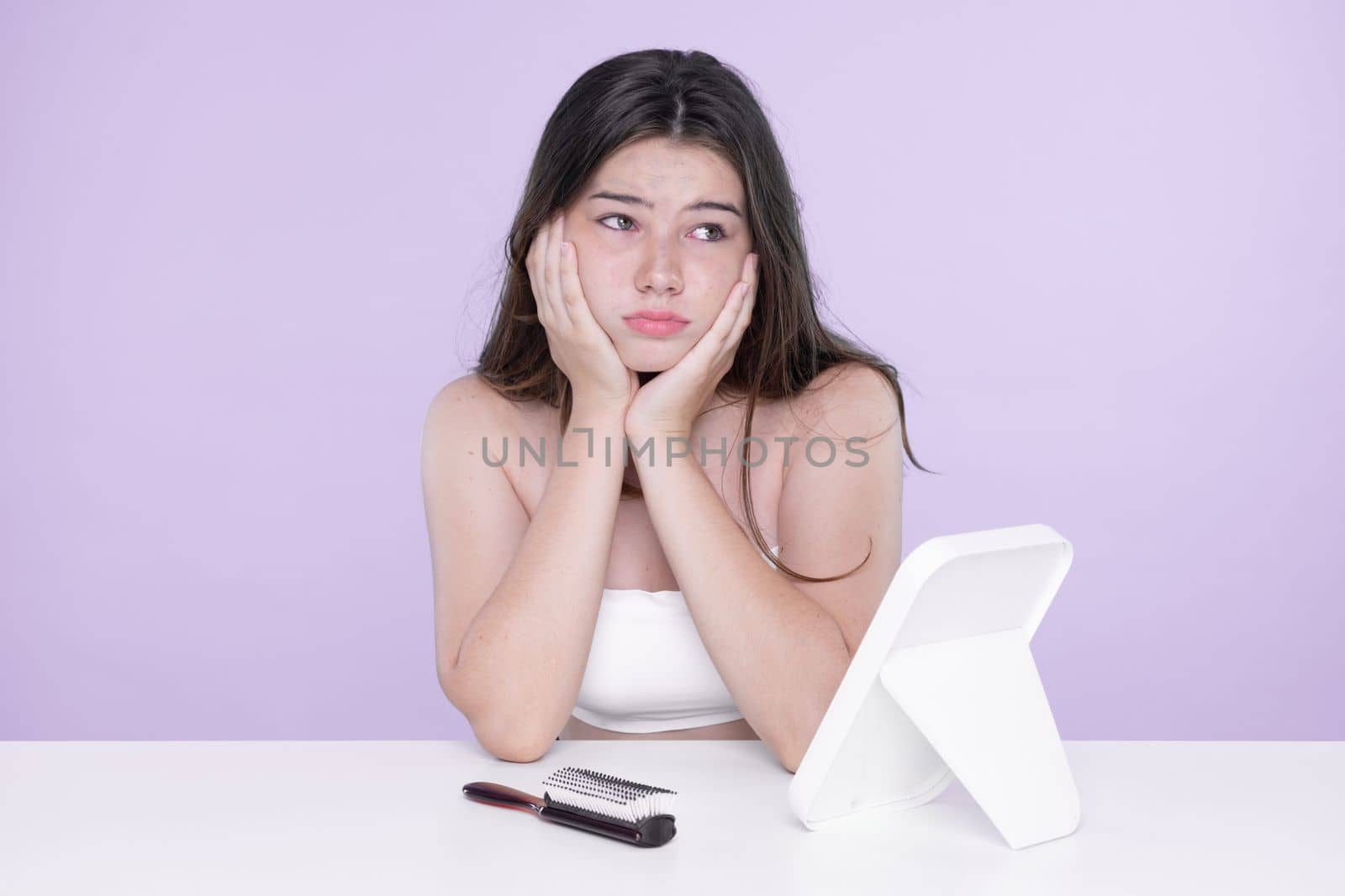 Young charming teenager girl worry about her face pimples on mirror for skincare and acne problem concept. Stress young girl squeezing pimples and pointing fingers on acne on her face.
