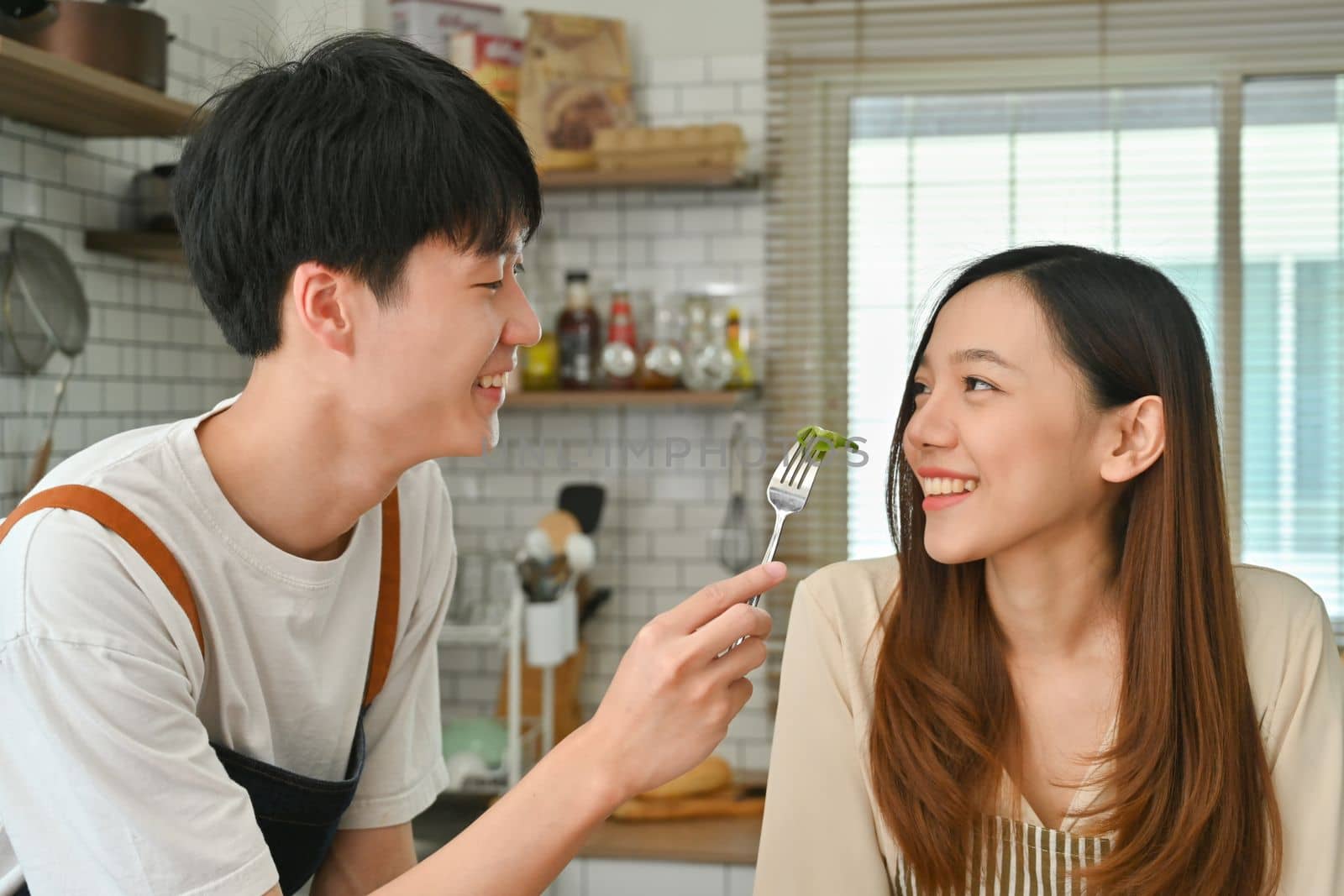 Happy young couple eating vegetable vegetarian salad together in the kitchen. Family moments, healthy lifestyle concept.