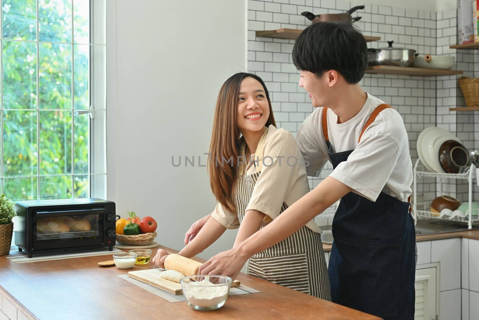 Cheerful young couple wearing aprons preparing homemade pastry, enjoying leisure time together at home.