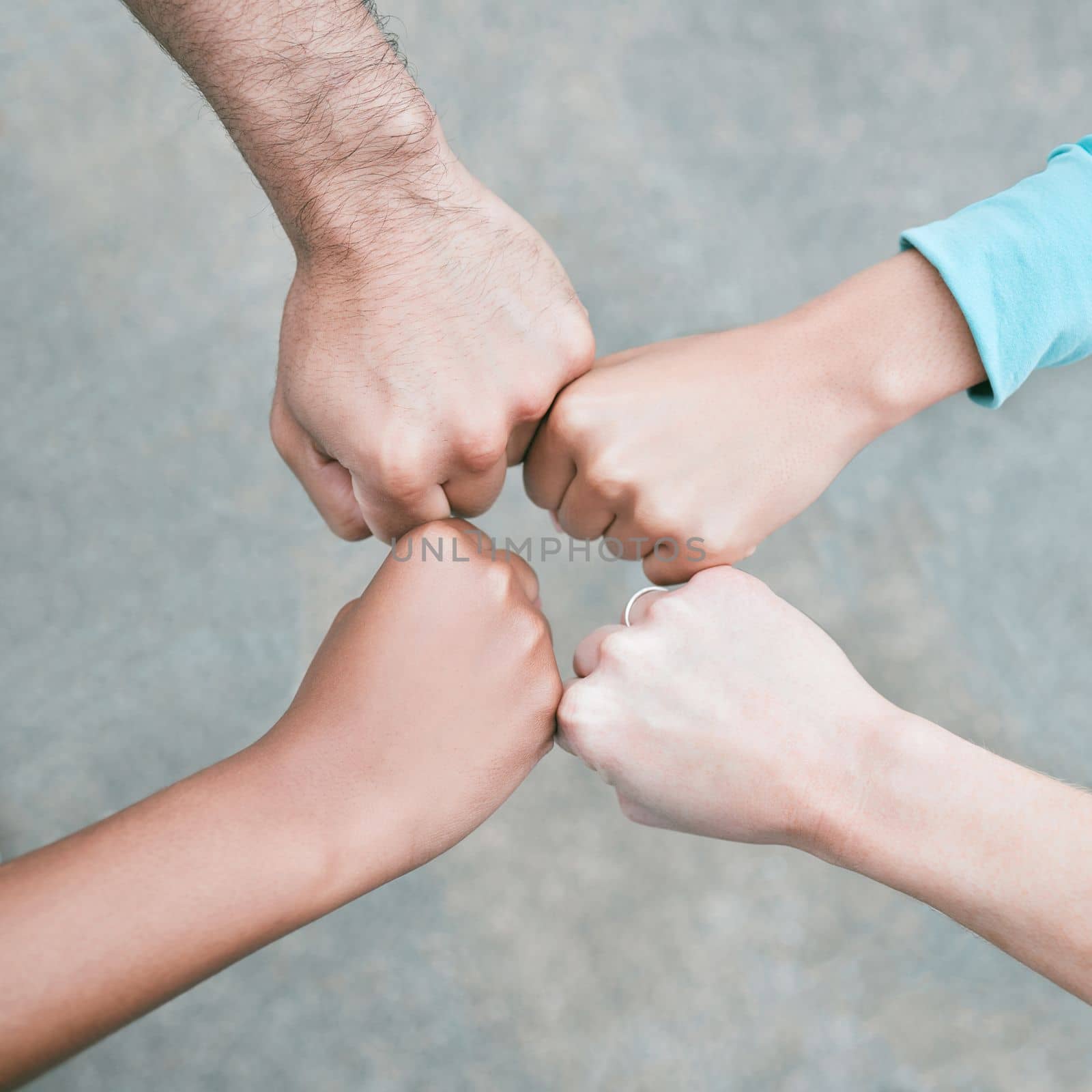 Closeup of diverse group of people from above making fists in a circle to express unity, support and solidarity. Hands of multiracial community greeting with fist bump in a huddle. Society joining to.
