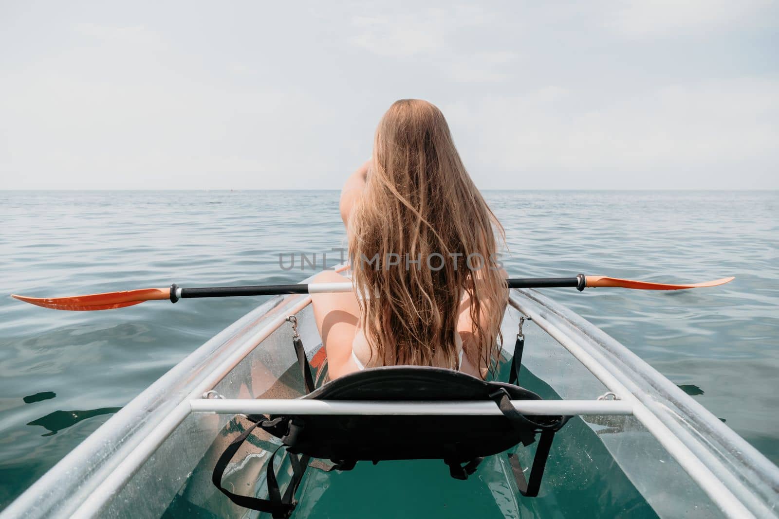 Woman in kayak back view. Happy young woman with long hair floating in transparent kayak on the crystal clear sea. Summer holiday vacation and cheerful female people having fun on the boat.