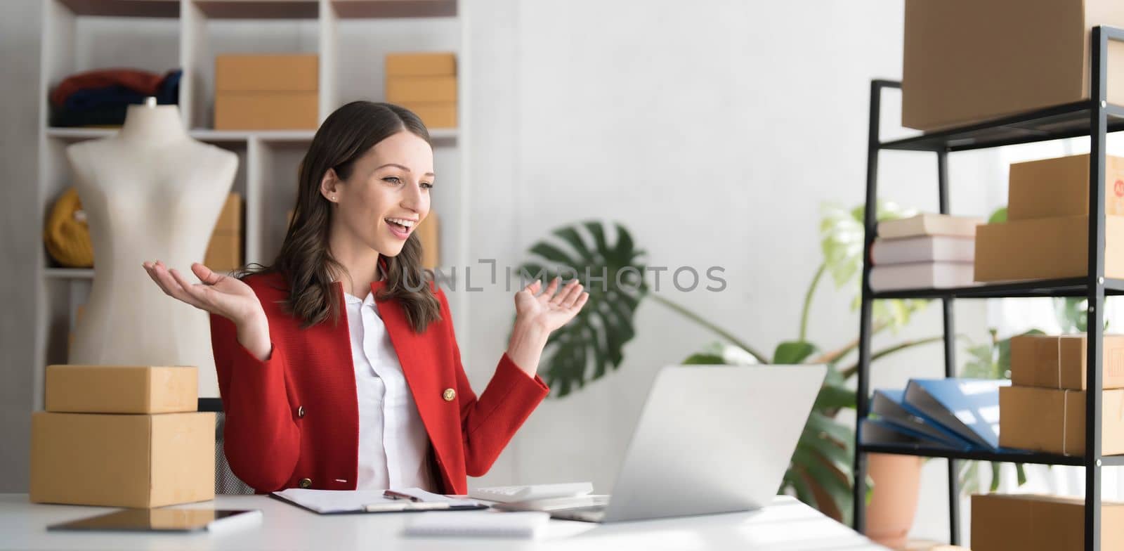 Smiling business owner working on laptop for livestreaming on social media, selling online. by wichayada