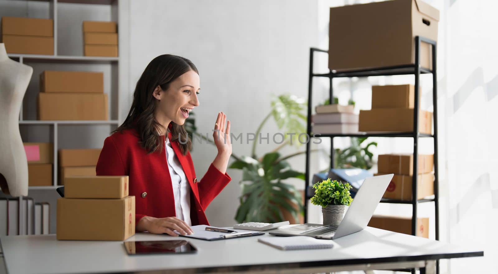 Smiling business owner working on laptop for livestreaming on social media, selling online. by wichayada