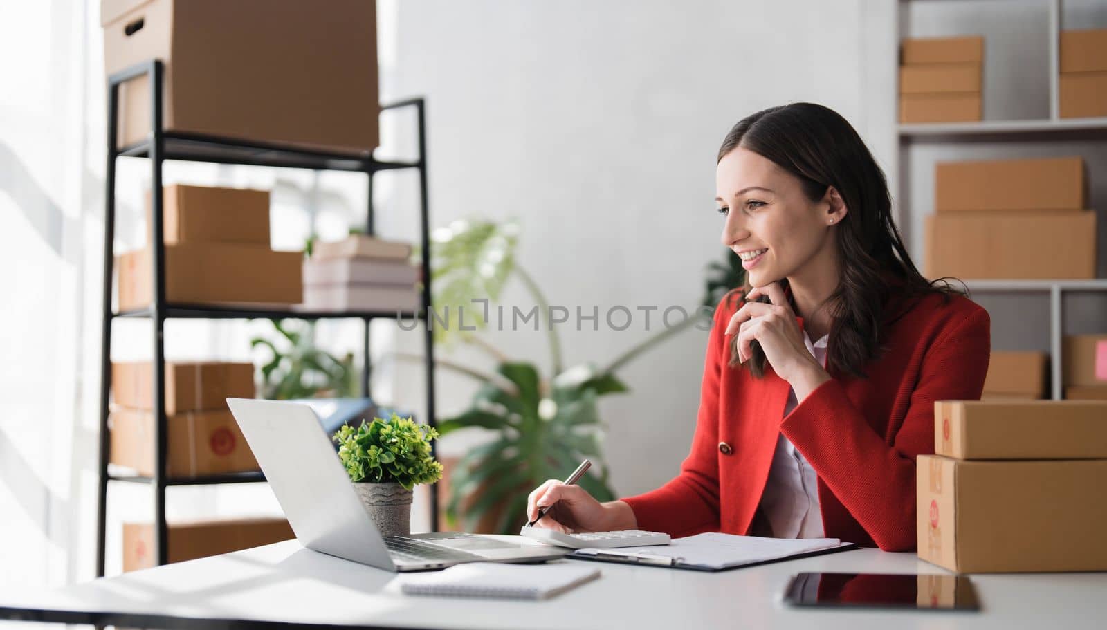 Entrepreneur using calculator with pencil in her hand, calculating financial expense at home office,online market packing box delivery,Startup successful small business owner, SME, concept by wichayada