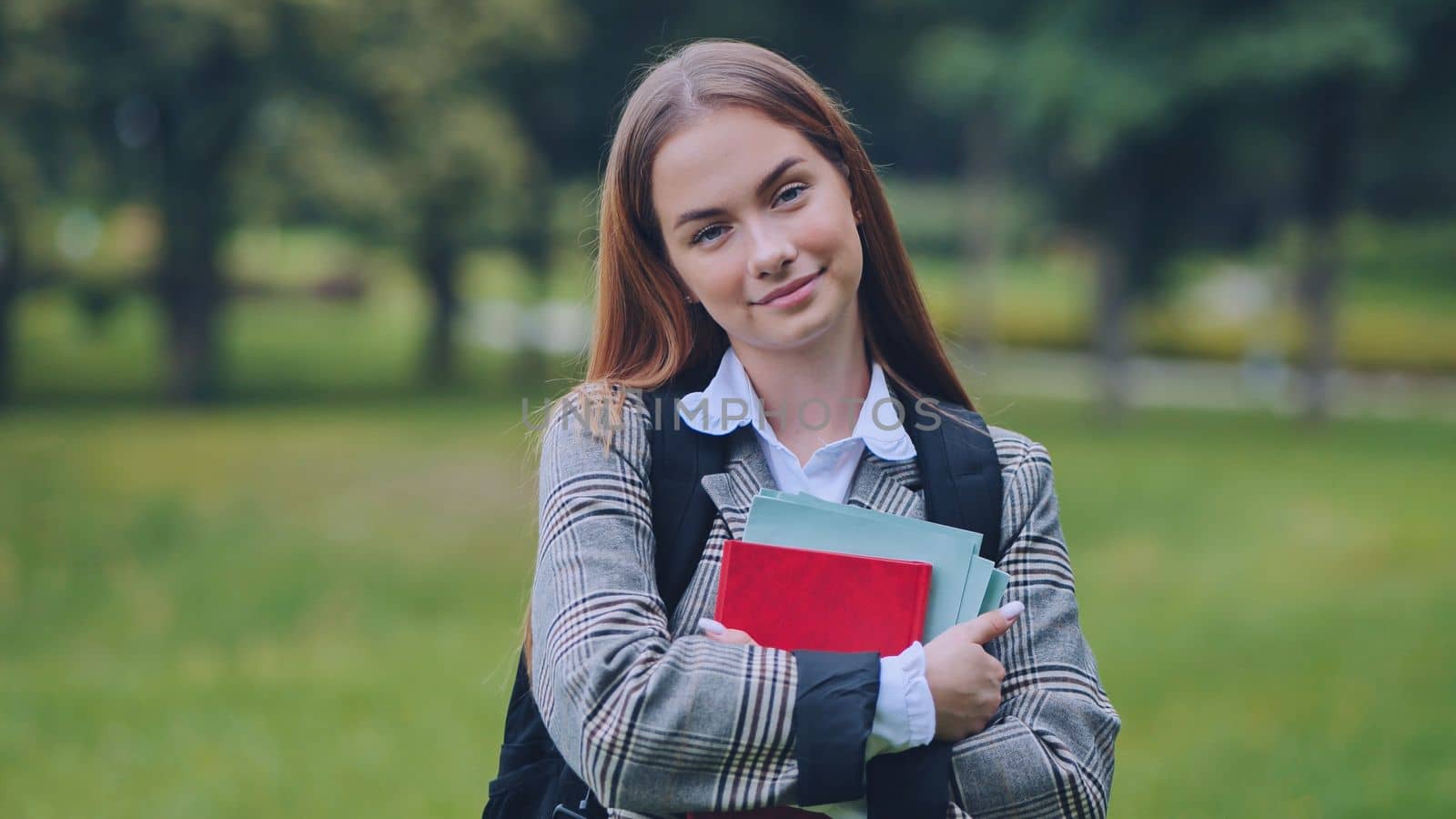 A smiling student with books in the park