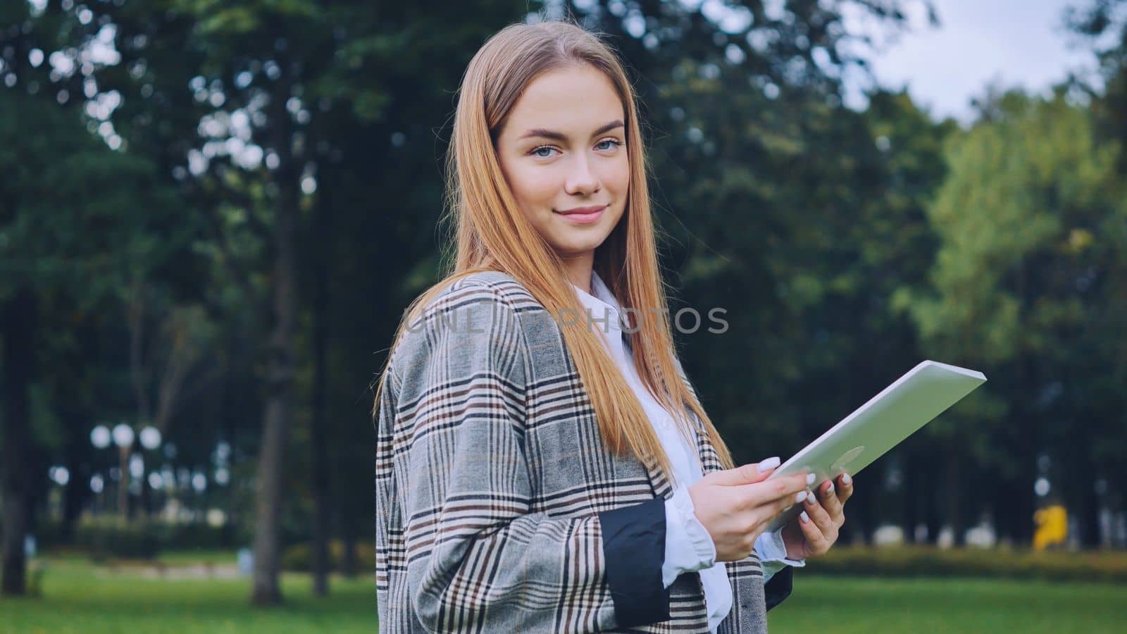 A young girl walks with a tablet in the park