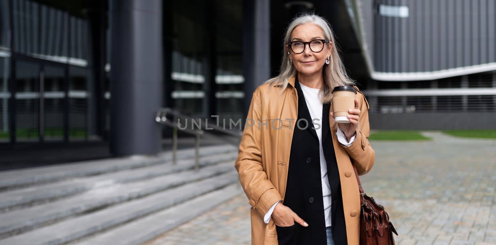 mature caucasian woman with a cup of coffee in her hands on the background of the shopping center by TRMK