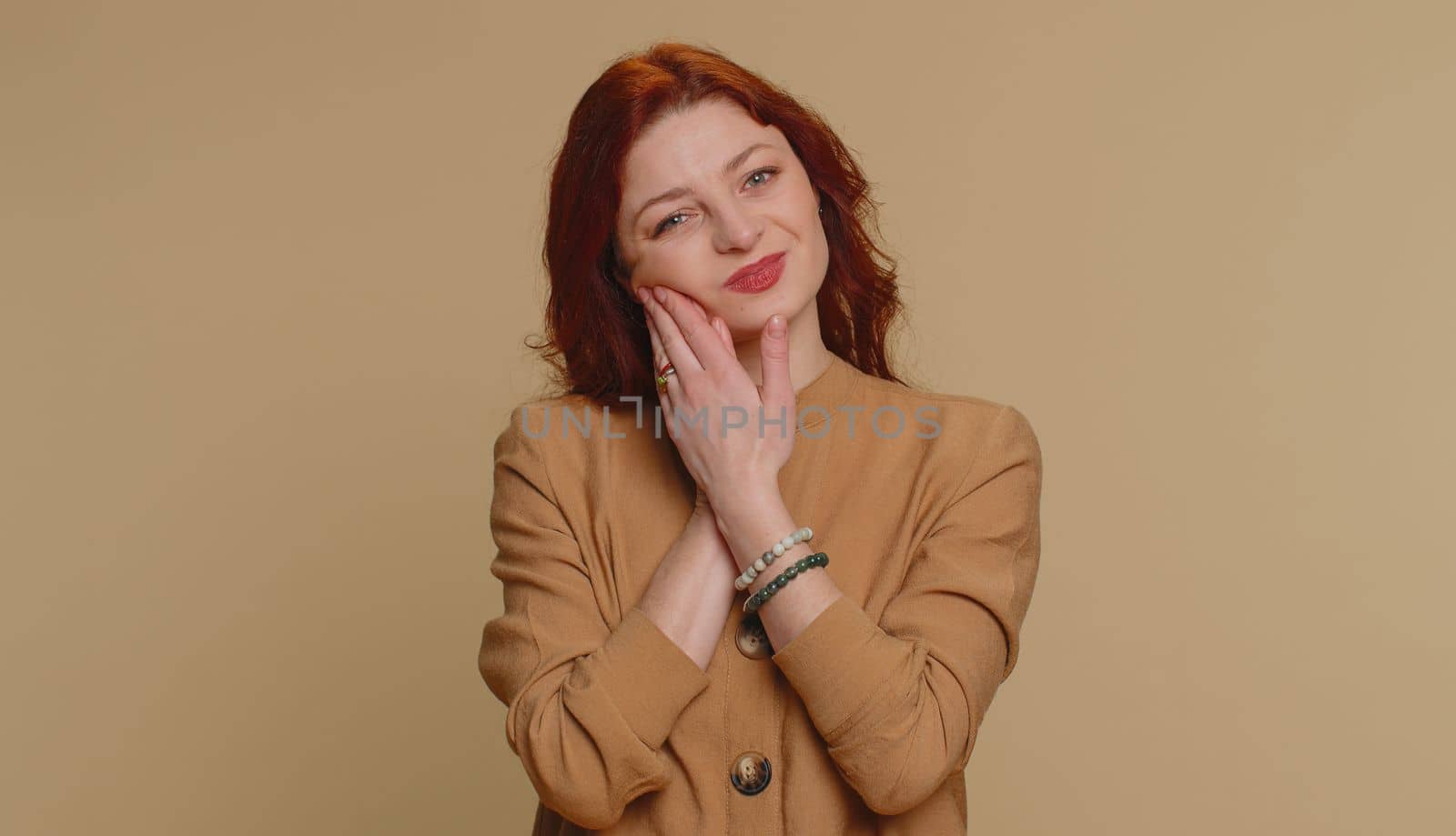Hipster redhead woman touching sore cheek suffering from toothache cavities or gingivitis waiting for dentist appointment gums disease. Young girl indoor studio shot isolated alone on beige background