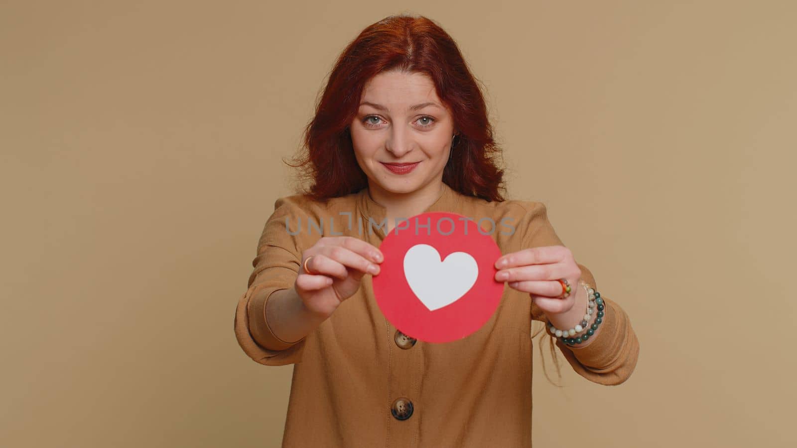 Like. Hipster pretty redhead woman show heart banner inscription agrees with something, gives positive reply recommends advertisement likes good. Young girl isolated alone on beige studio background