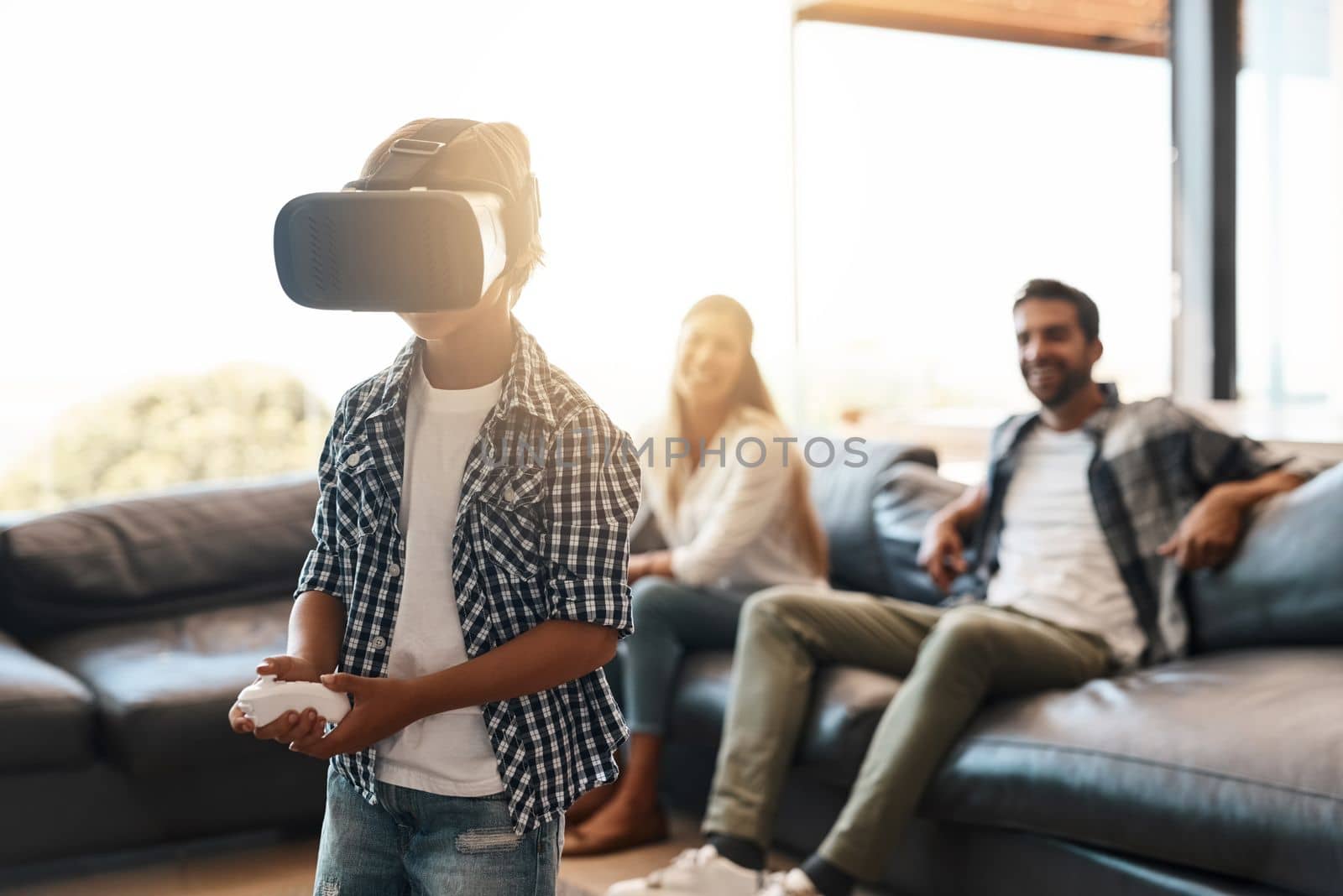 Its a whole new world were living in. a little boy using a virtual reality headset at home with his parents in the background. by YuriArcurs