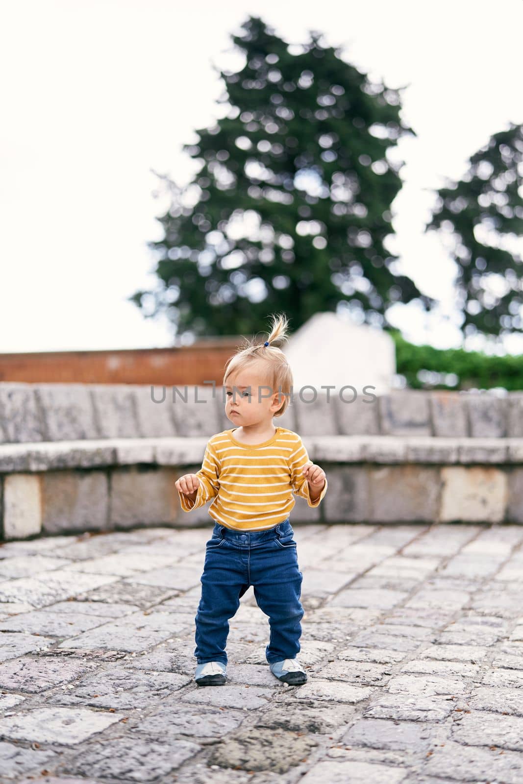 Little girl stands on a stone platform in the park and looks to the side by Nadtochiy