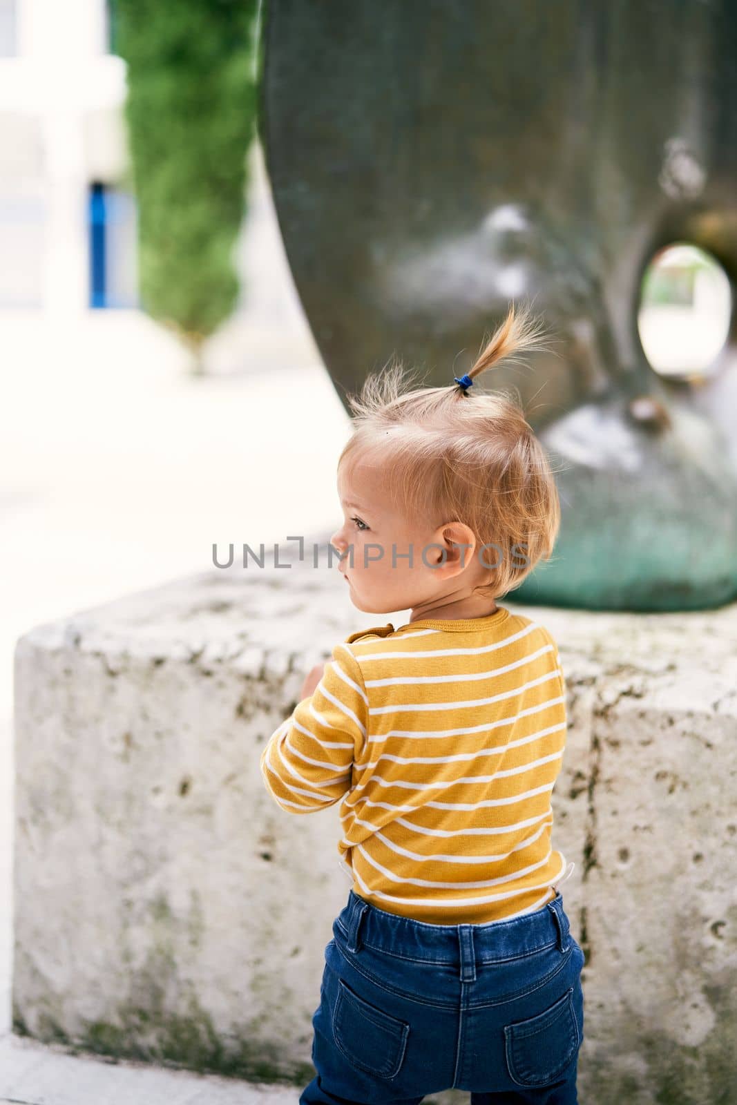 Little girl stands in front of the sculpture with her head turned to the side. Back view. Close-up. High quality photo