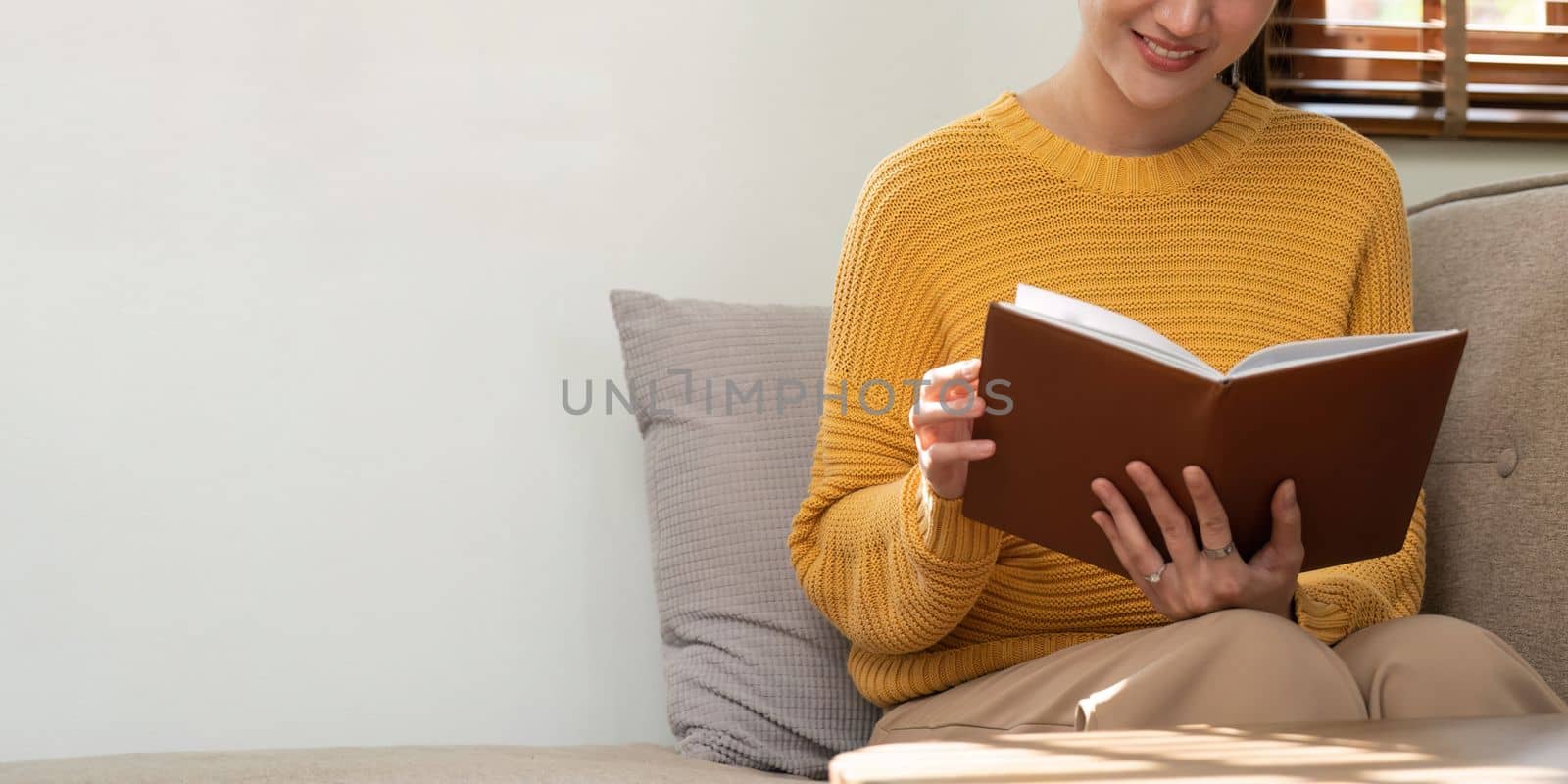 Happy and relaxed Asian woman reading a book on sofa.