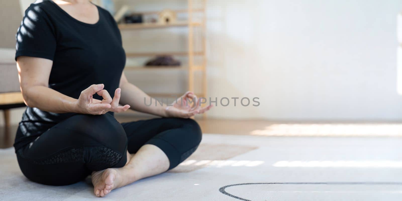 Healthy and elderly woman in workout clothes practicing yoga in her living room by nateemee