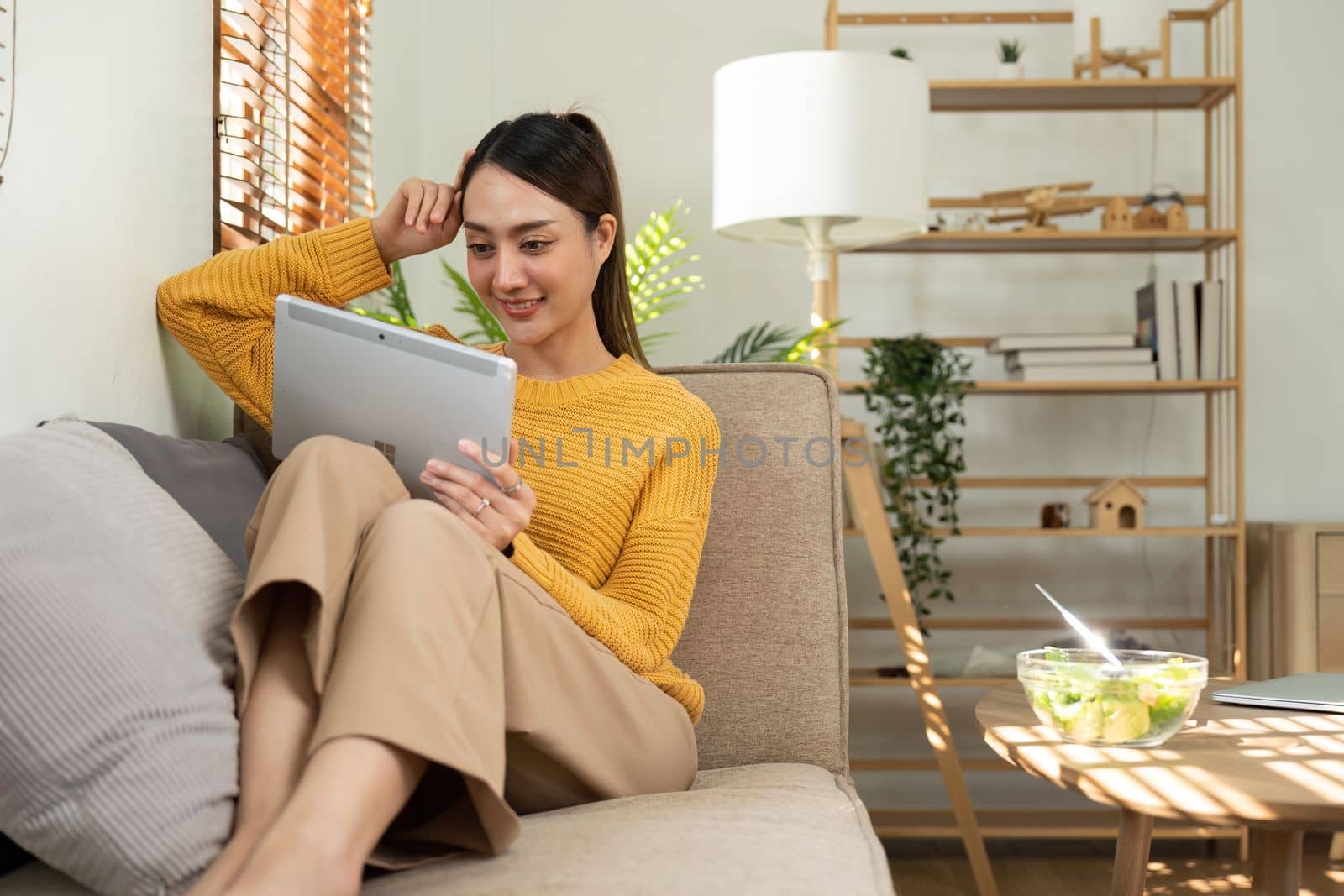 Happy Asian woman eating healthy salad vegetables mix while using her laptop in the living room. work from home.