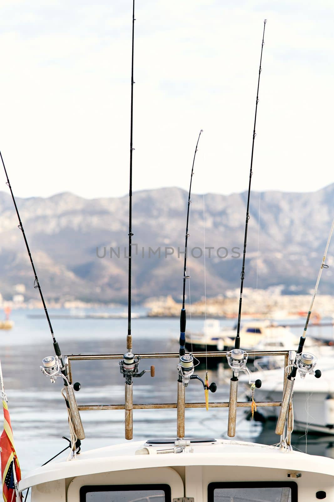 Fishing rods attached to the stern of a white yacht against the backdrop of a pier, boats, sea and mountains. Close-up. High quality photo