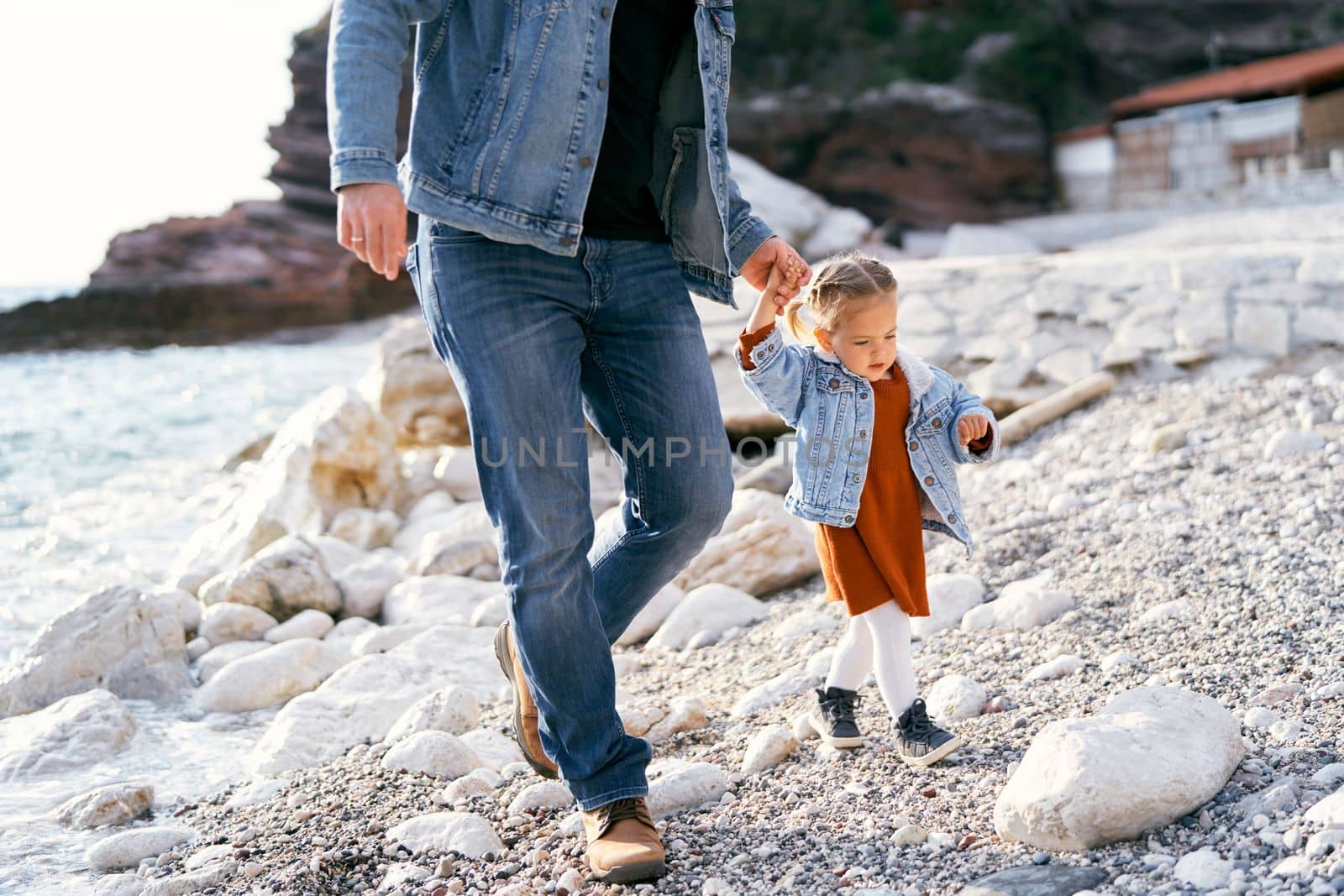 Dad leads a little girl by the hand over the stones on a pebble beach near the town of Rafailovici, Montenegro. Close-up. High quality photo