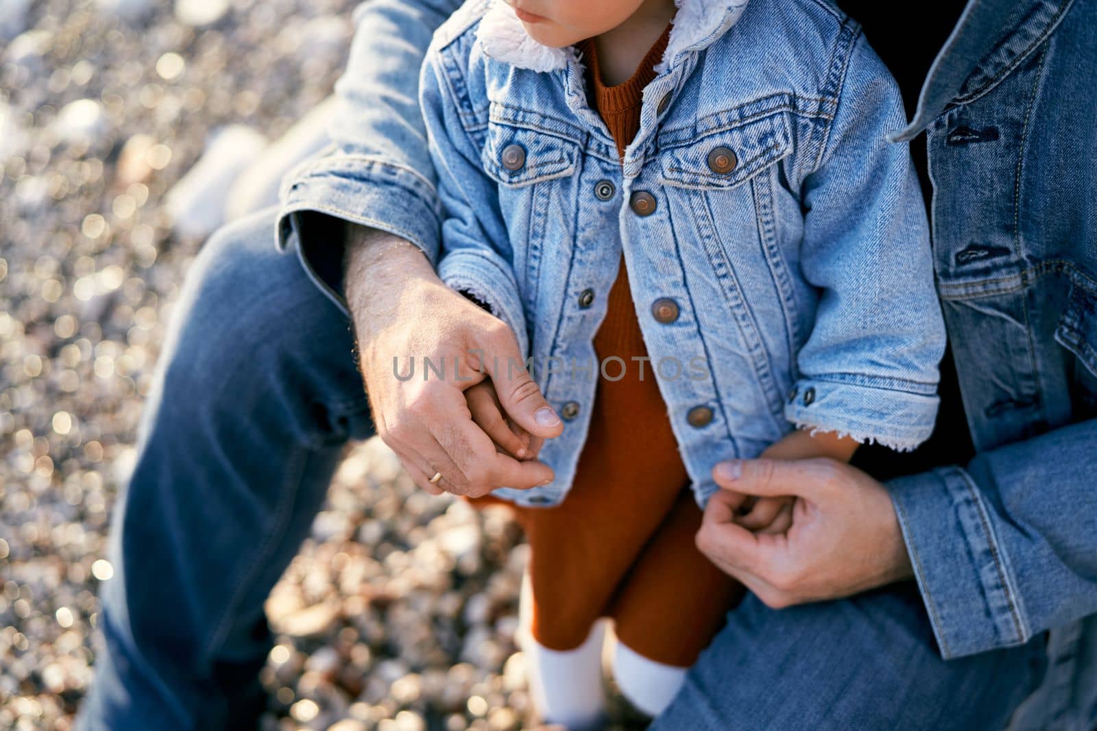 Dad sits and hugs a little girl on a pebble beach. Close-up. High quality photo