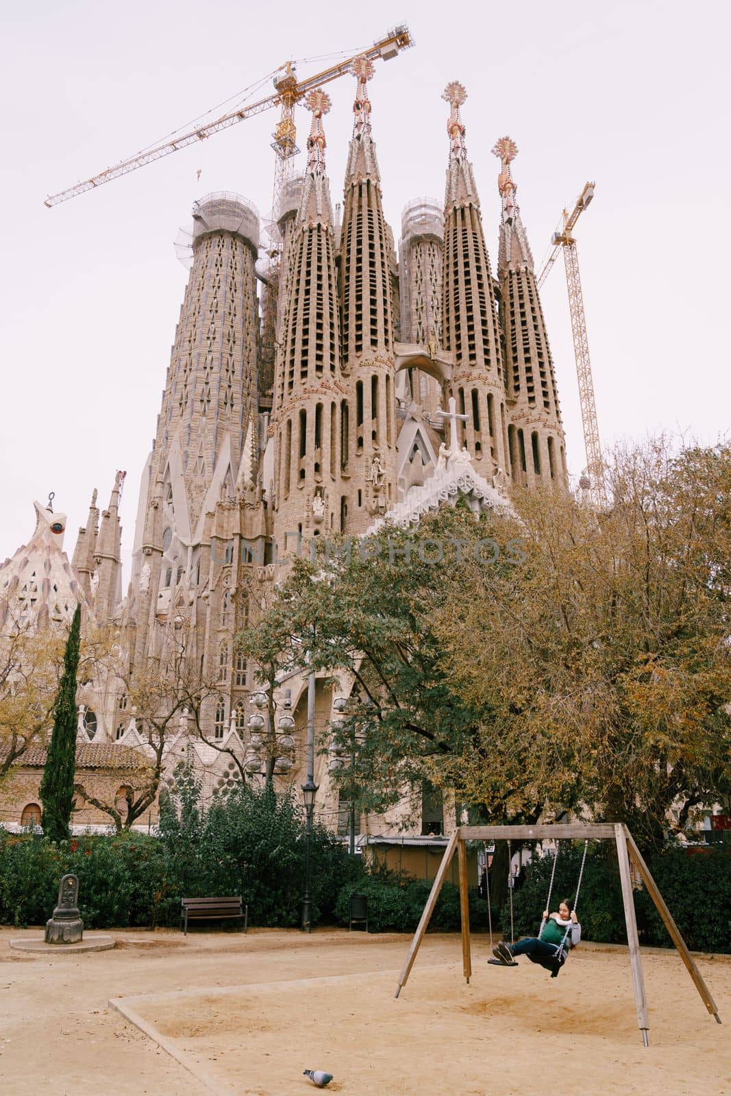Mom with a baby in her arms swinging on a swing against the background of the Sagrada Familia church, Barcelona, Spain. High quality photo