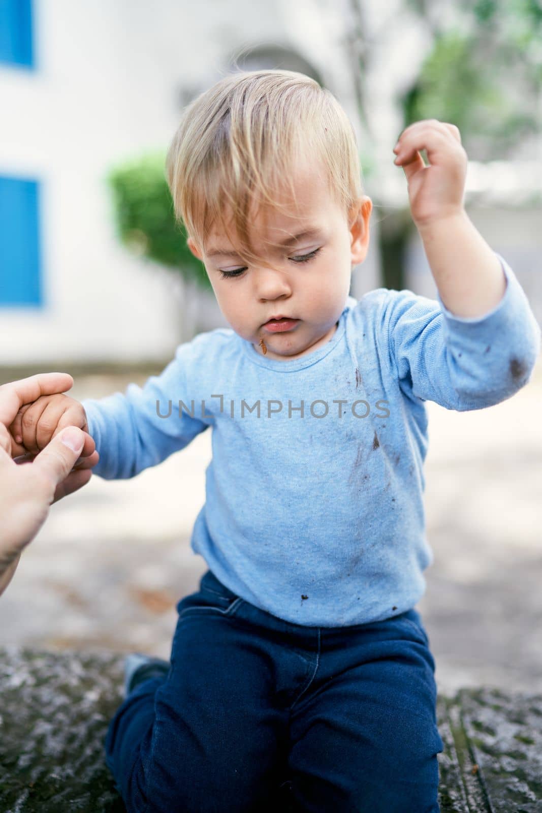 Kid sits on a stone fence in the yard with his hands up. High quality photo