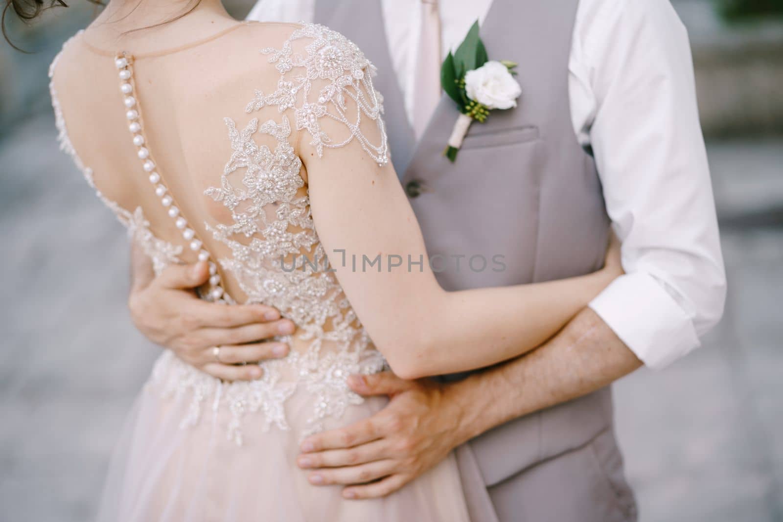 Hands of groom on the waist of bride in an embroidered lace dress. Close-up. High quality photo