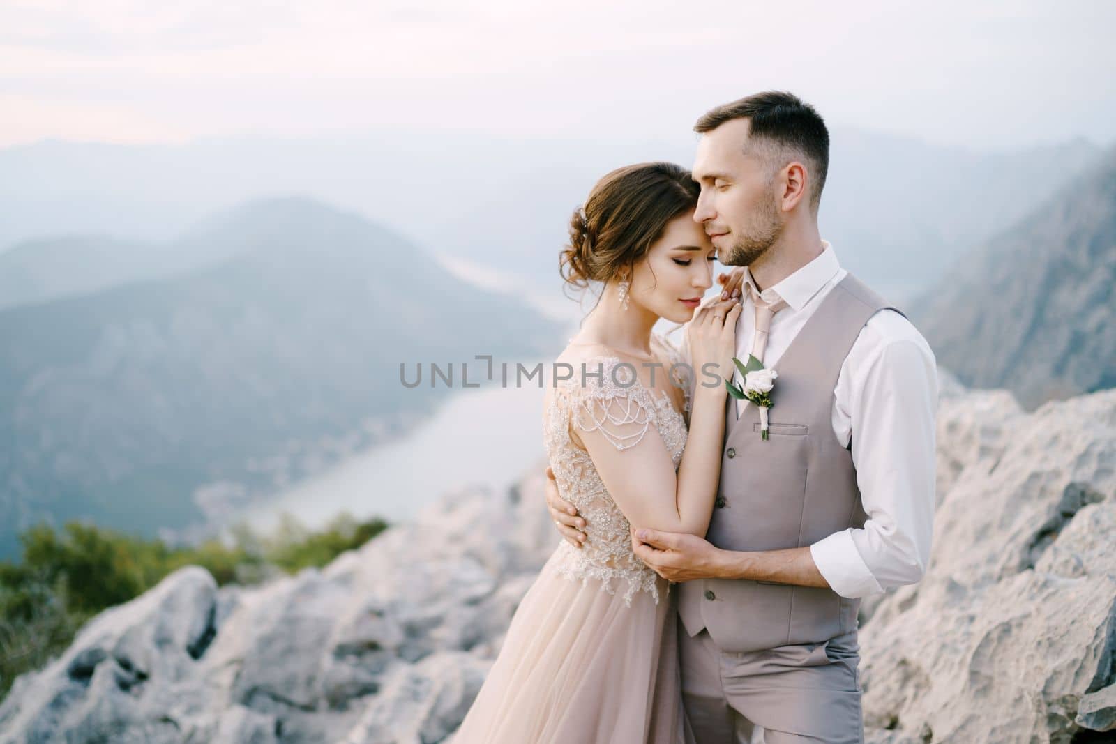 Groom hugs bride on the mountain on the background of Kotor Bay. High quality photo