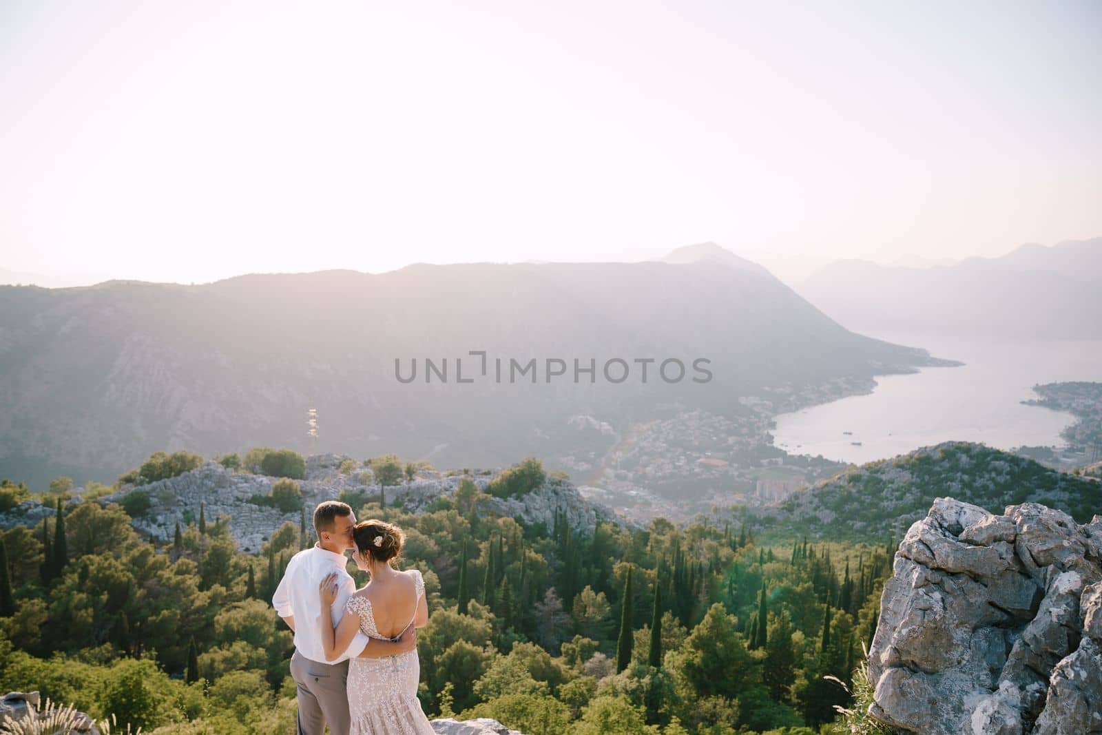 Groom hugs the bride on a high mountain against the backdrop of a panorama of the bay and trees. High quality photo