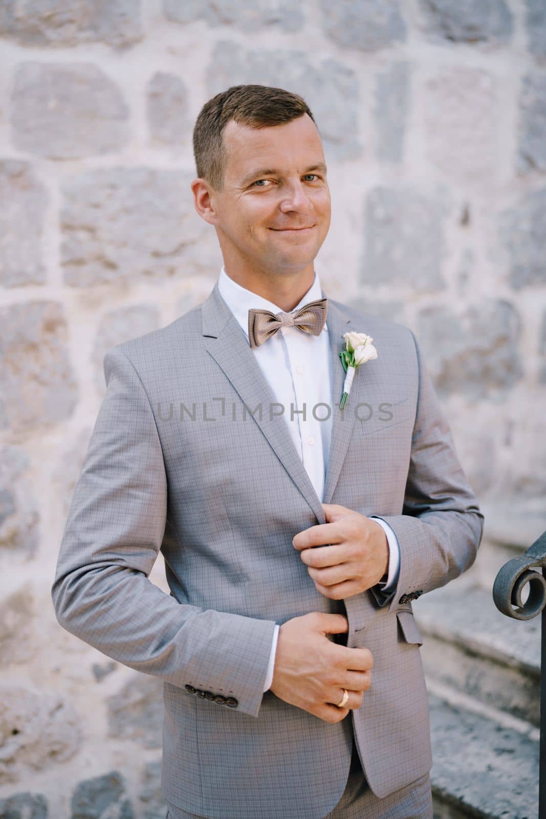 Groom holds the lapels of his jacket with his hands and stands on the stone stairs. High quality photo
