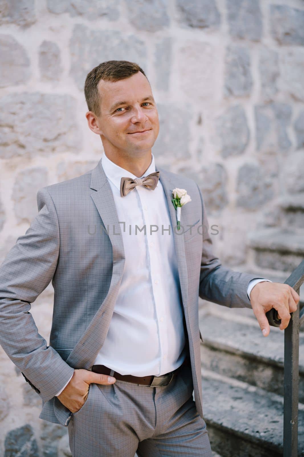 Groom stands on a stone staircase with his hand on the handrail. High quality photo