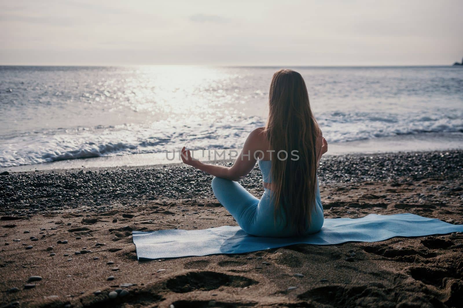 Middle aged well looking woman with black hair doing Pilates with the ring on the yoga mat near the sea on the pebble beach. Female fitness yoga concept. Healthy lifestyle, harmony and meditation.