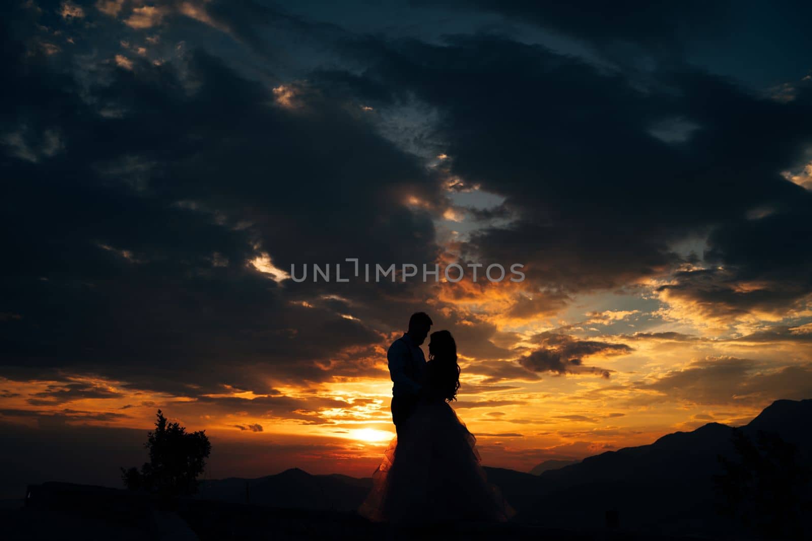 Silhouettes of the bride and groom who are embracing on Mount Lovcen overlooking the Bay of Kotor at sunset . High quality photo
