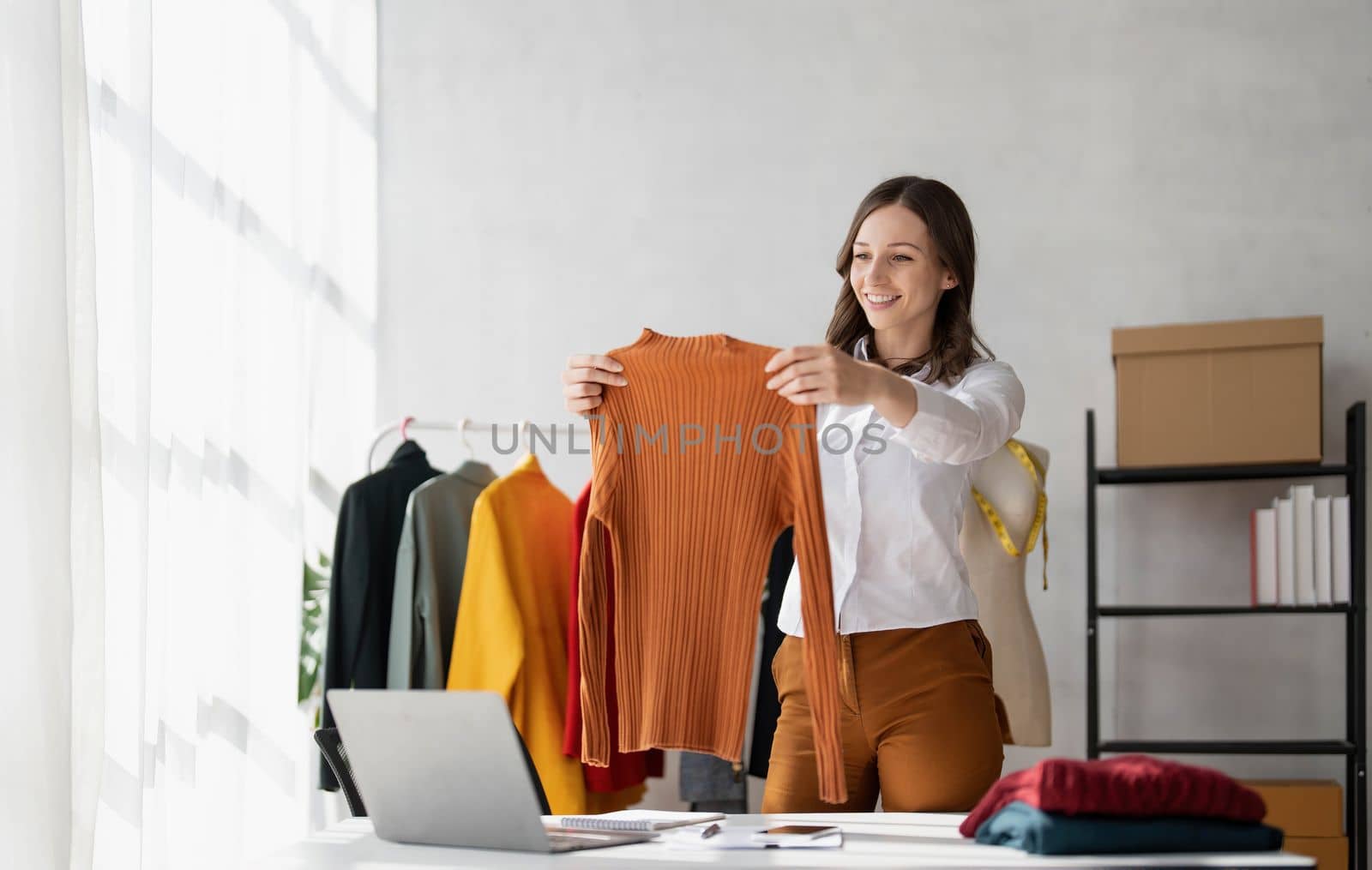 Portrait of young beautiful asian woman fashion designer is picking up shirts to compare proportions for customers to view them online. by wichayada