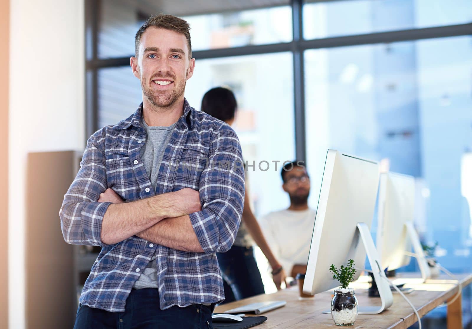 This is a great company to work for. Portrait of a confident young businessman standing in an office with his team in the background