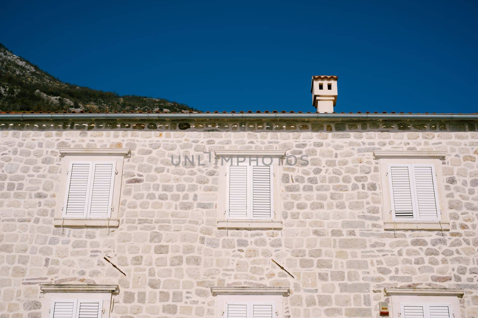 Gray stone building facade with white shutters on the windows. High quality photo
