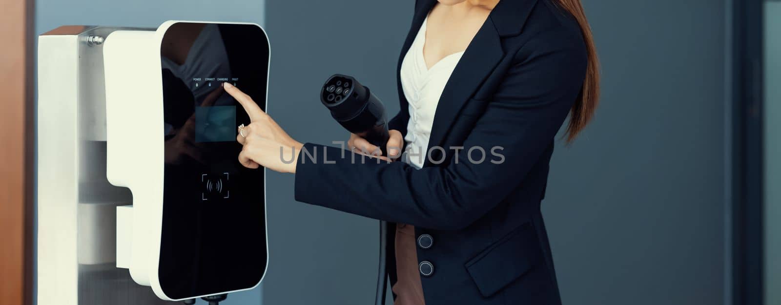 Closeup asian woman holding and pointing an EV plug, a home charging station providing a sustainable power source for electric vehicles. Alternative energy for progressive lifestyle.