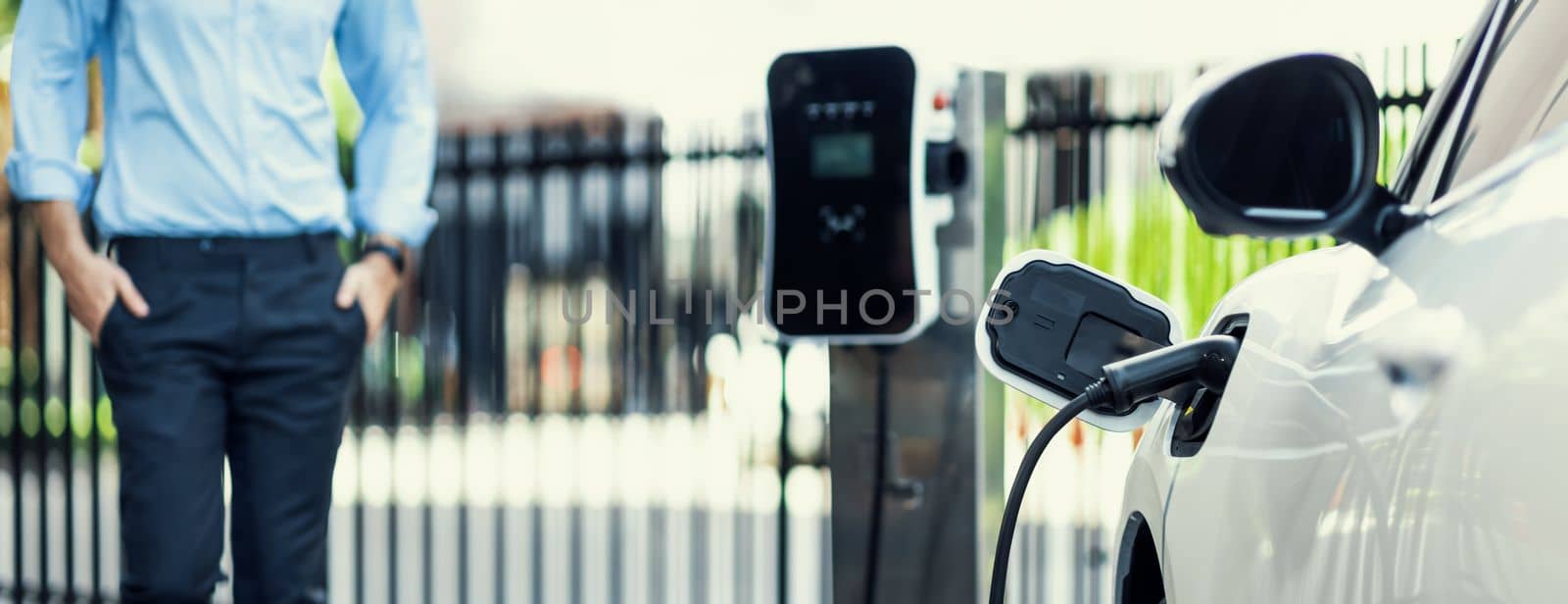 Closeup progressive businessman with electric vehicle at charging station. by biancoblue