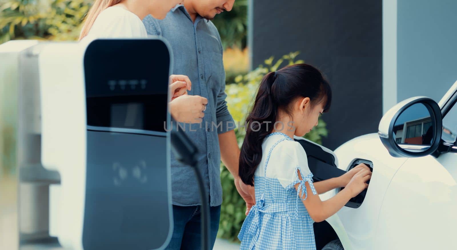 Progressive young parents and daughter living in a home with an electric car. by biancoblue