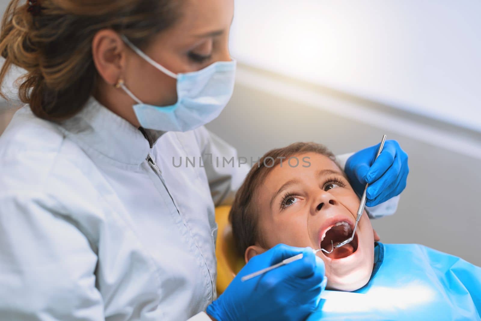 No pain and no stress. a young little boy lying down on a dentist chair while getting a checkup from the dentist. by YuriArcurs