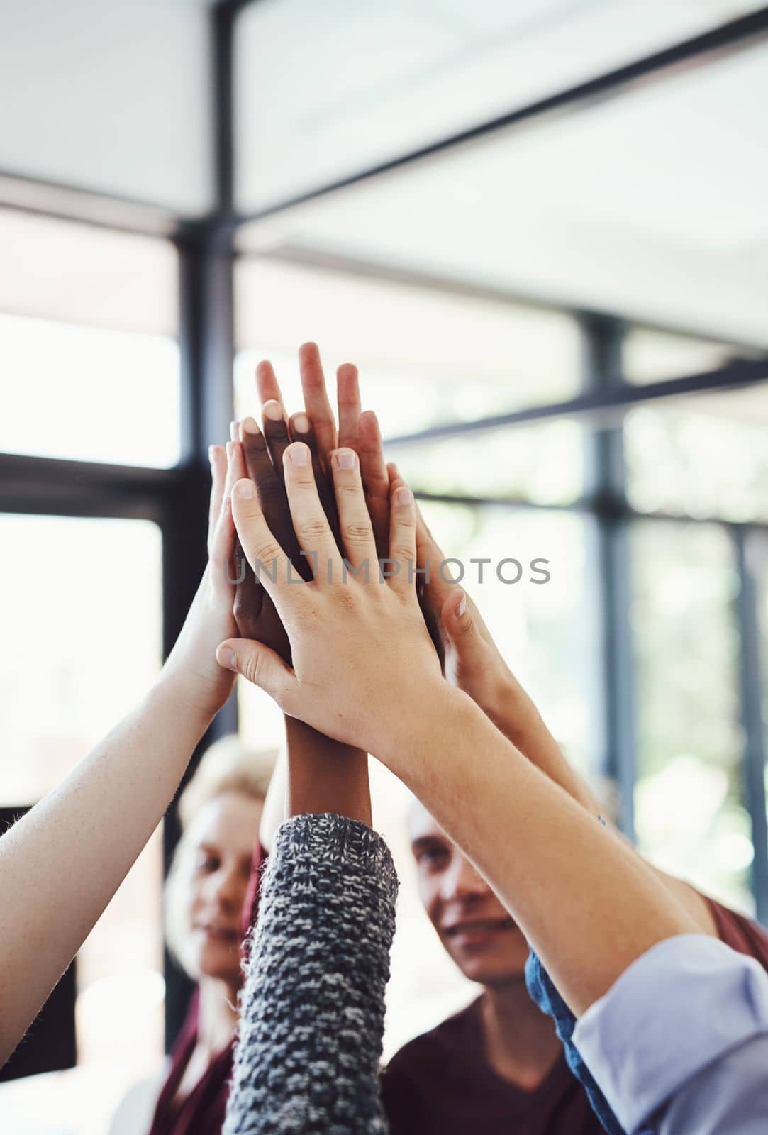 Heres to teamwork. a group of people high-fiving in the office. by YuriArcurs